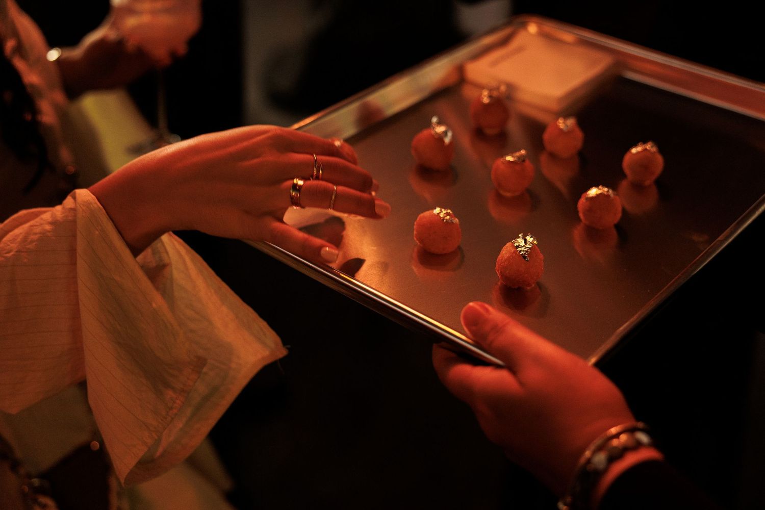 Hands reaching for small appetizers on a dark serving tray.