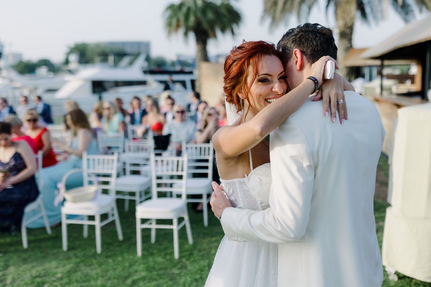 A romantic moment between a couple during an outdoor wedding ceremony with palm trees and white chairs.