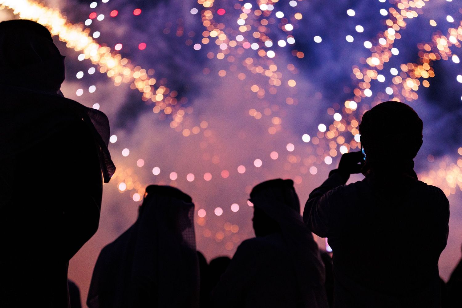 Silhouettes of people dancing under string lights at an outdoor party or celebration at dusk.