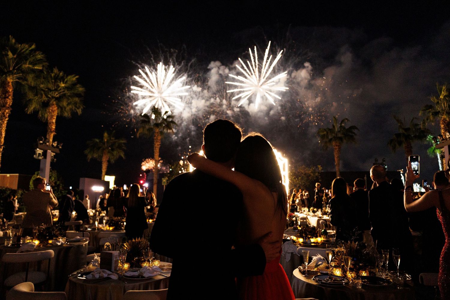 Silhouetted crowd watches spectacular fireworks display lighting up the night sky during an outdoor celebration.
