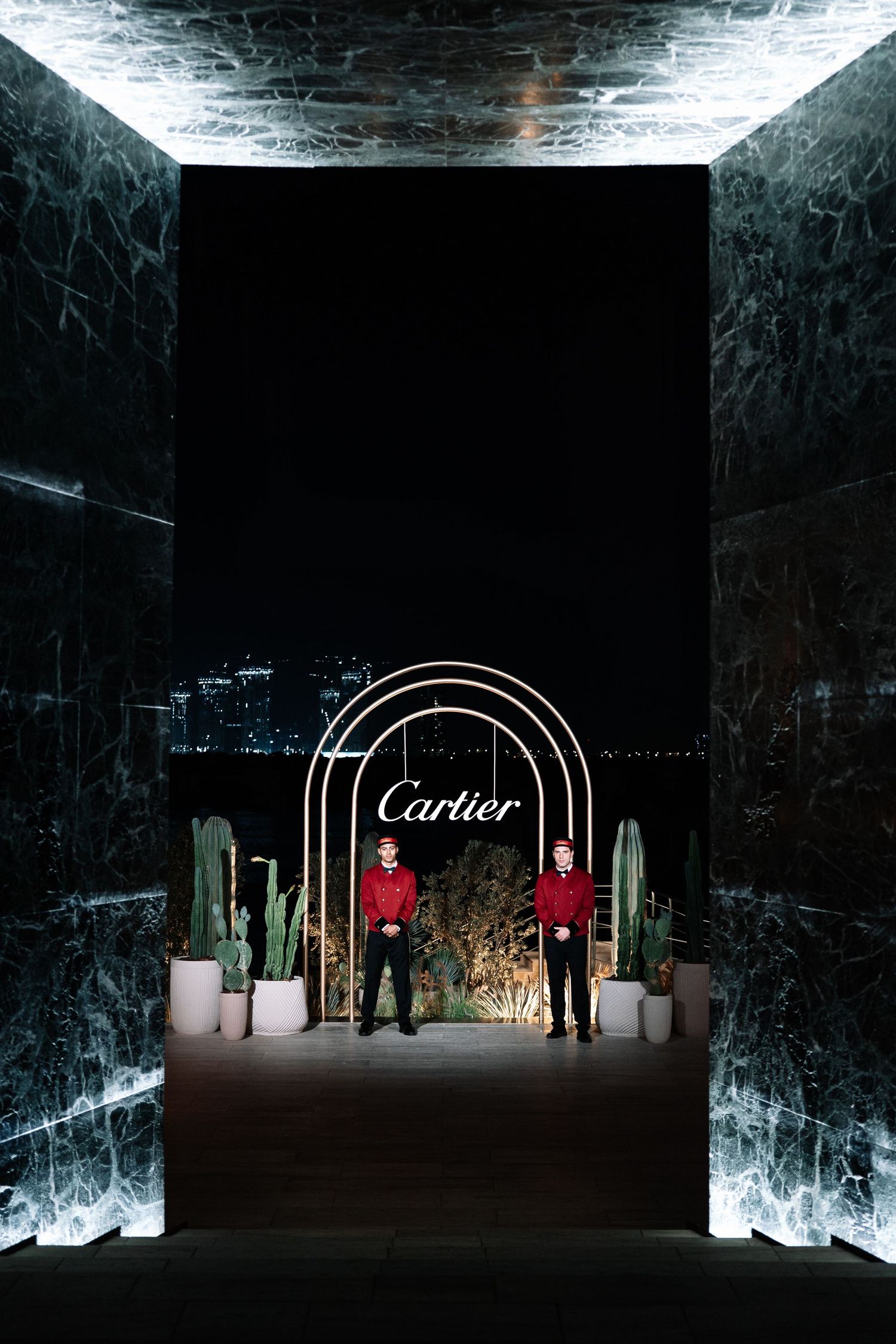 Dark marble exhibition space with illuminated Cartier logo and display pedestals creates dramatic luxury retail atmosphere.