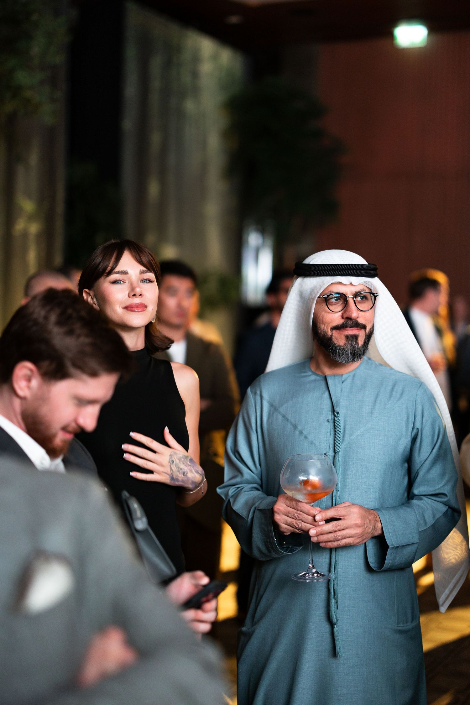 People in formal attire socialize at an evening event while holding drinks and engaging in conversation.