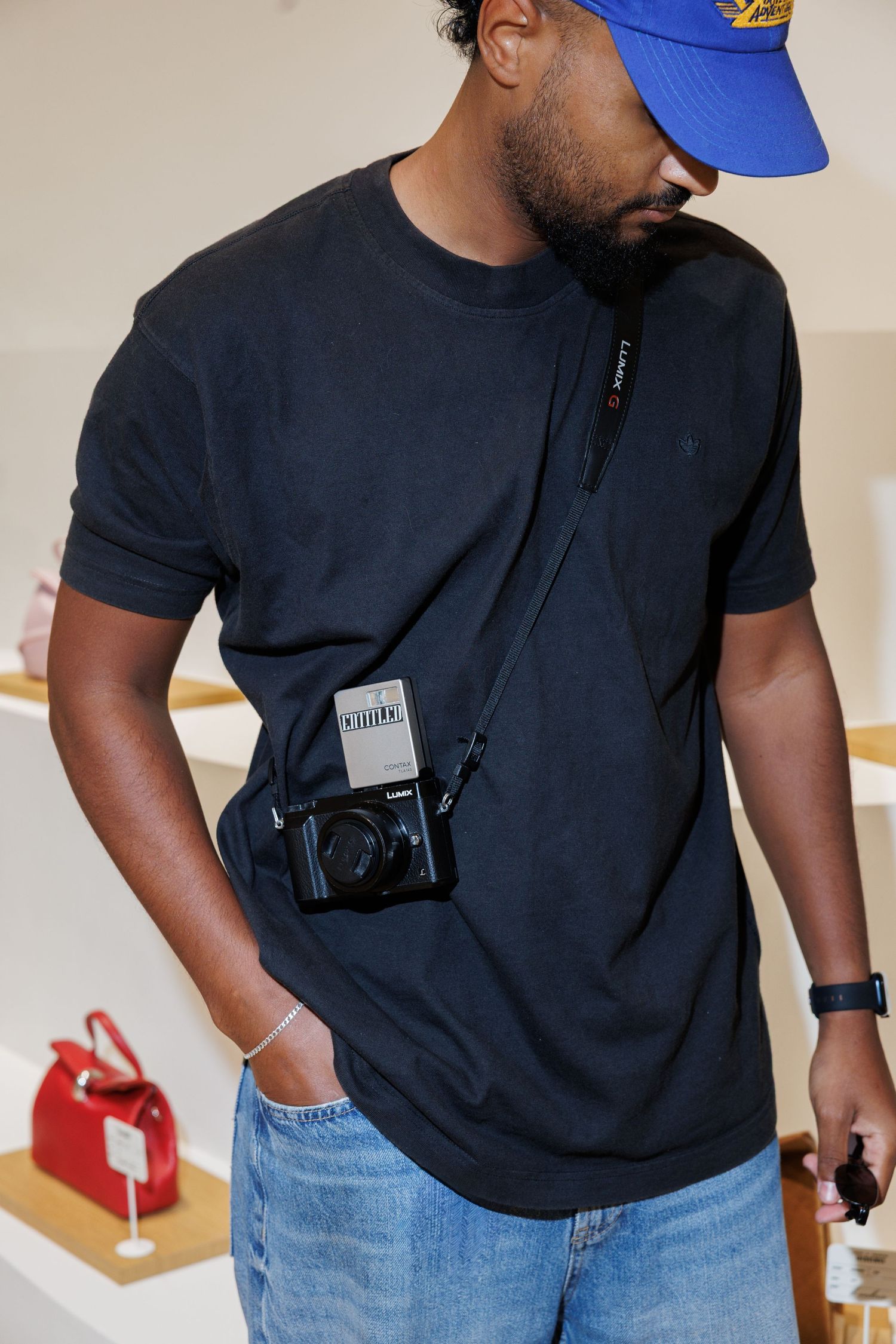 Person wearing a black t-shirt and blue jeans holding a camera in a retail space.
