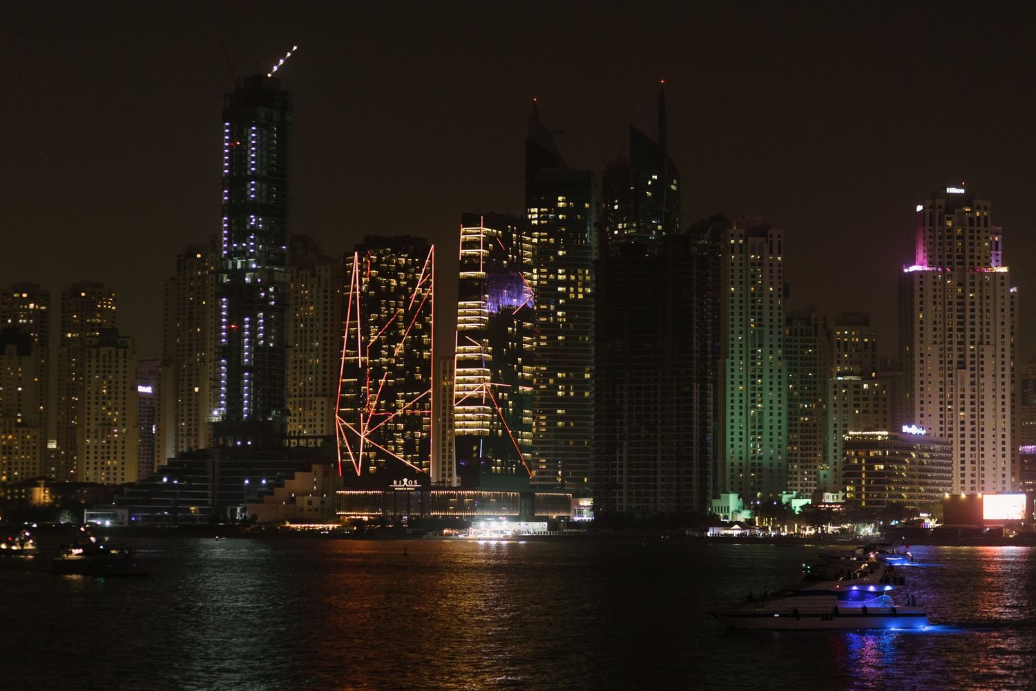 Illuminated Dubai skyline at night with modern skyscrapers reflecting on the water.