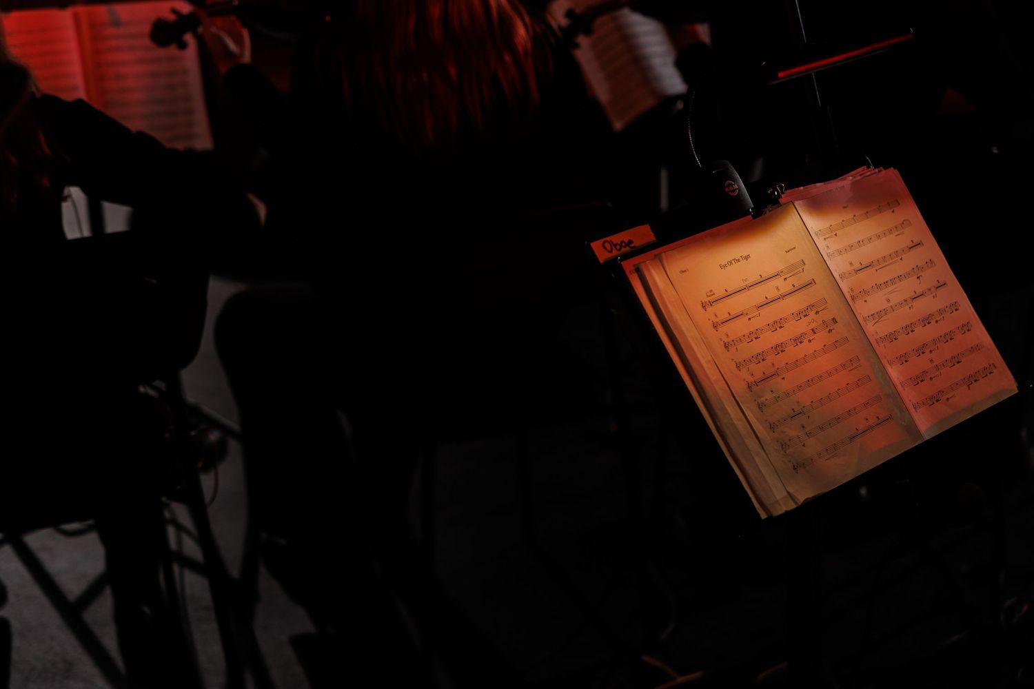 Music sheets on a dark stage lit with red theatrical lighting during a performance.
