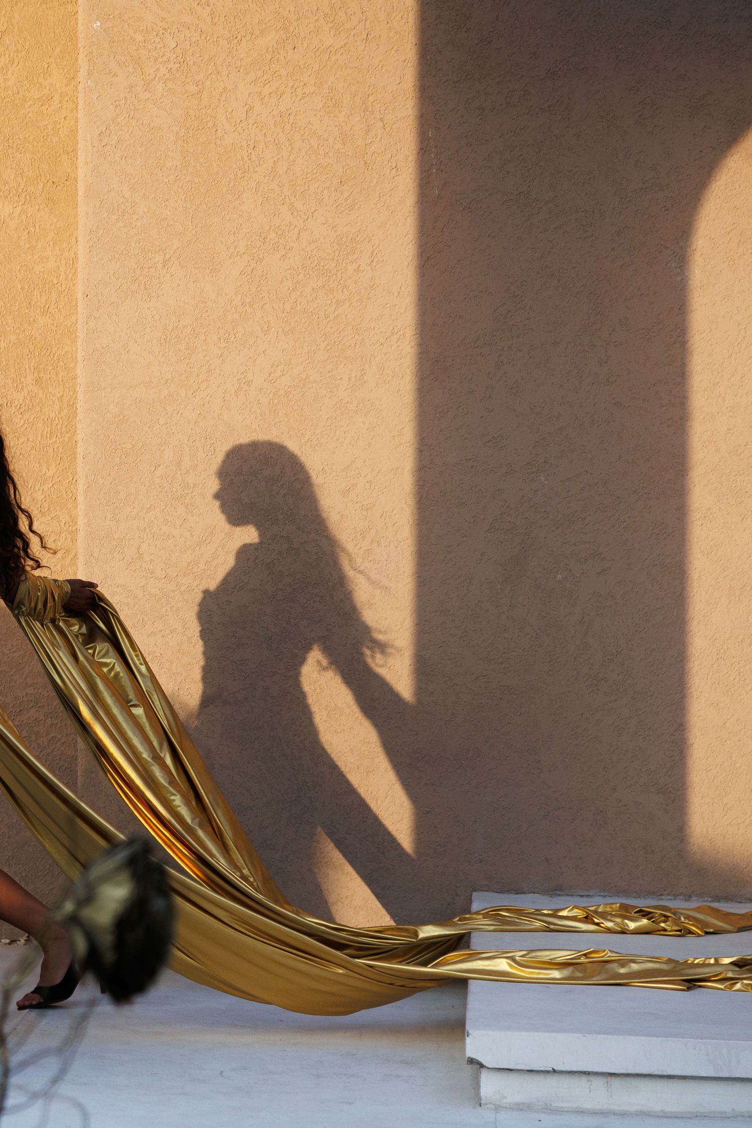 Dramatic shadows cast on beige wall with gold papers creating artistic composition.