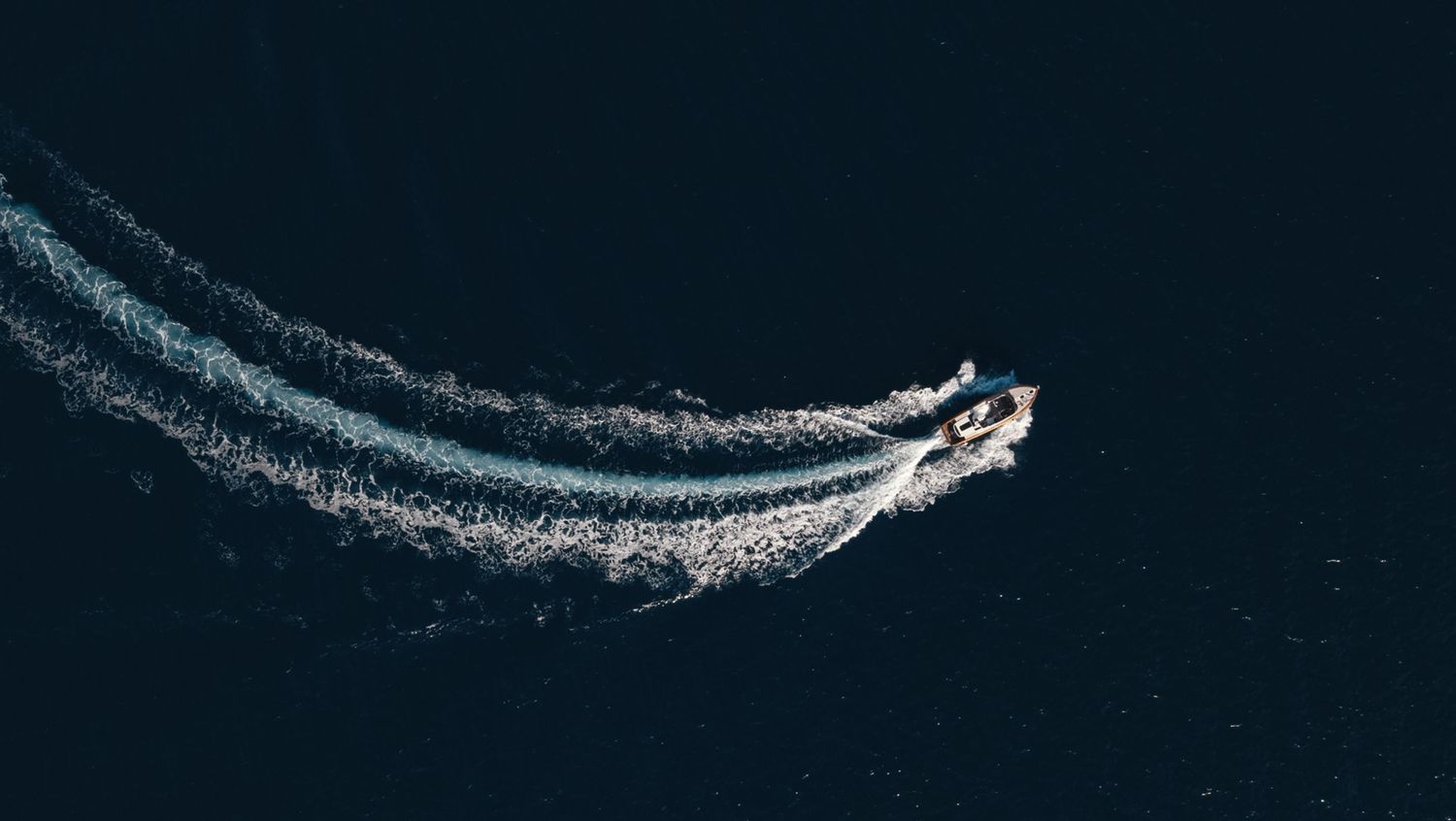 Aerial view of boat wake patterns creating curves in dark ocean water.