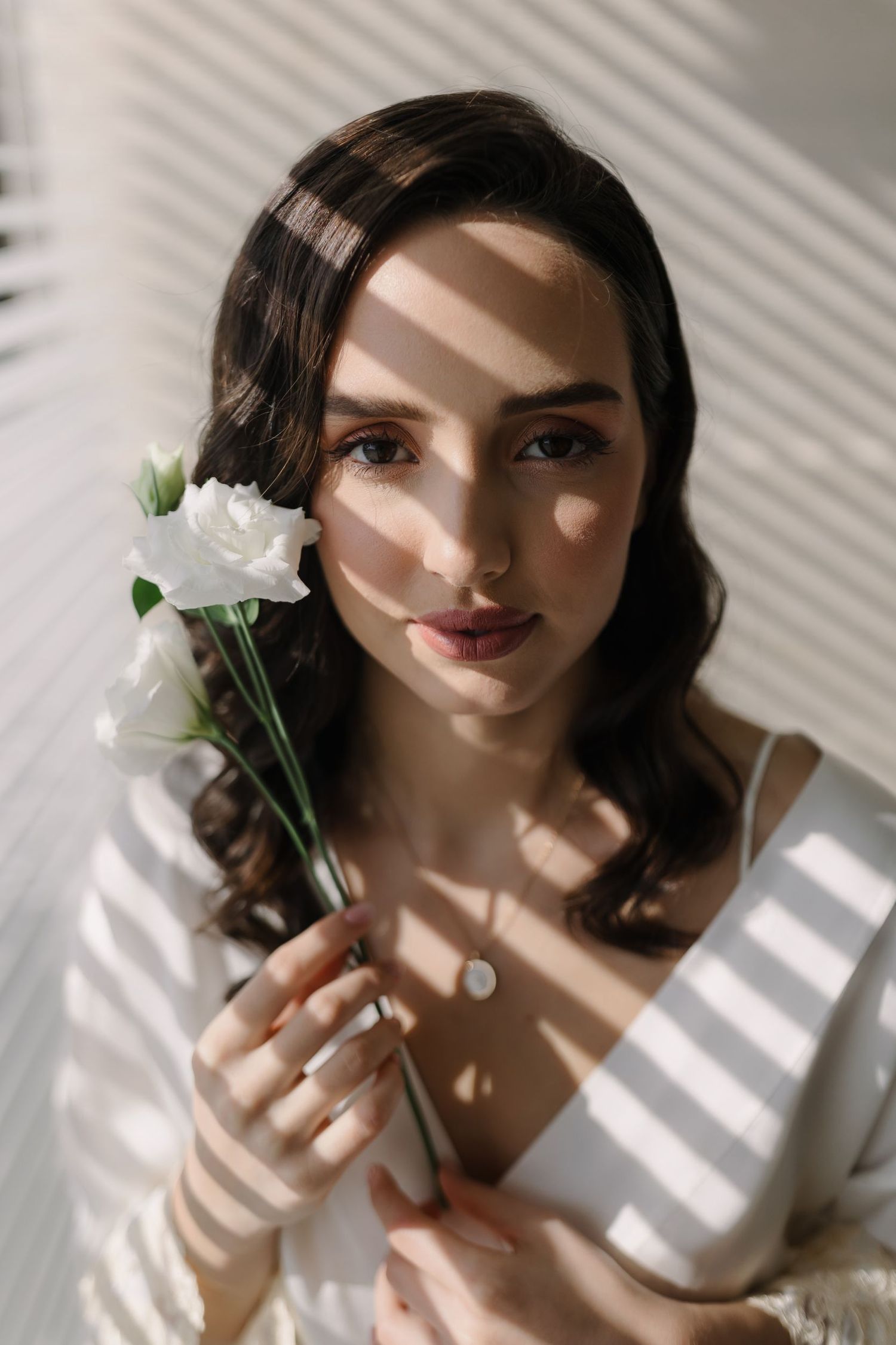Artistic portrait with dramatic window light and white flowers creating shadow patterns.