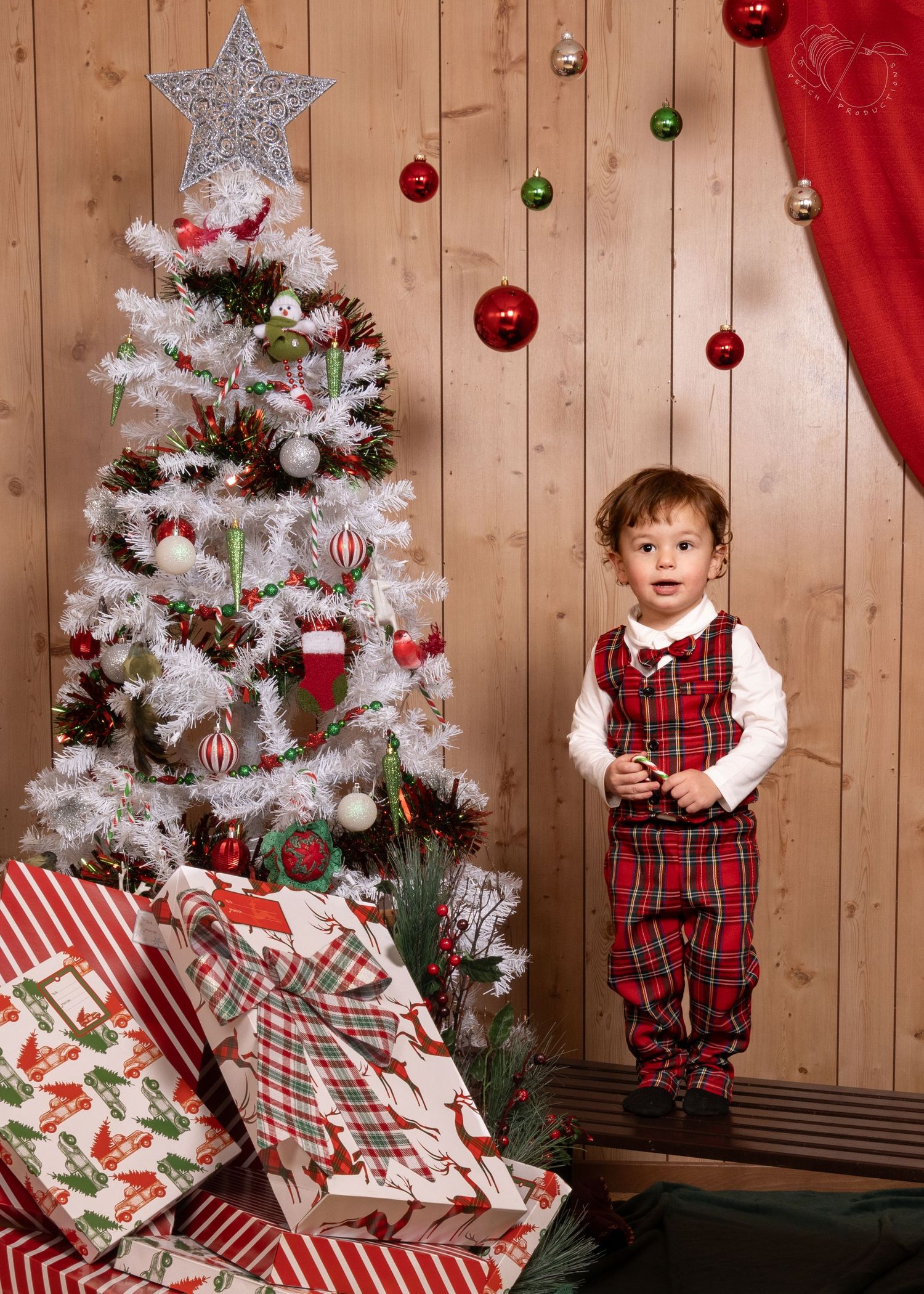 Children in matching plaid holiday outfits by white Christmas tree with wrapped presents.