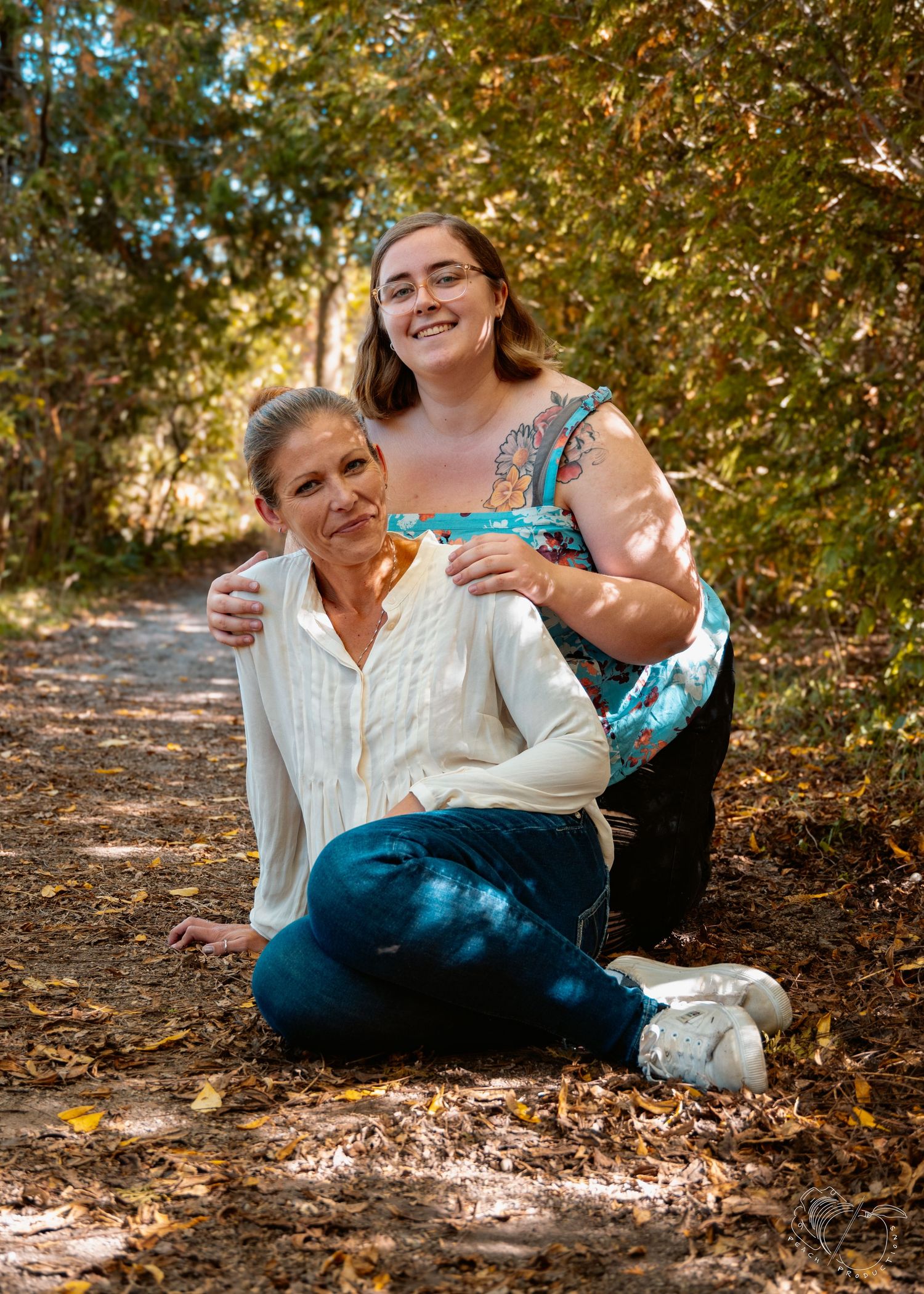 Two people relax and laugh together on a sunlit forest path in autumn.