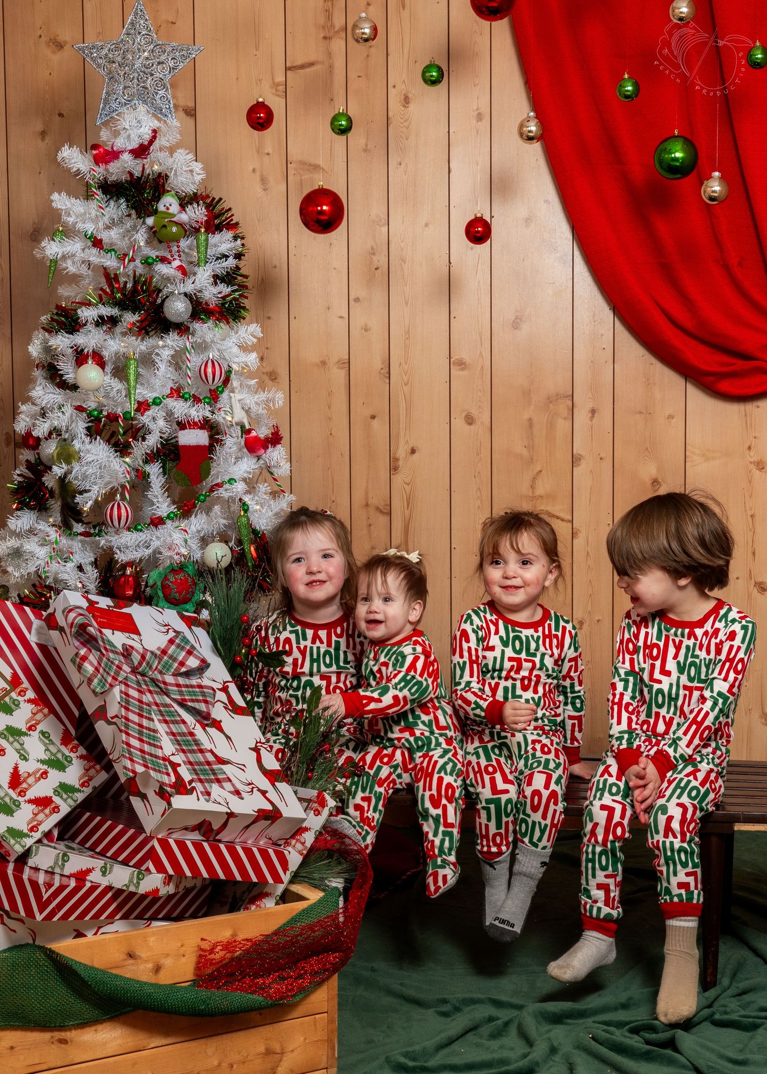 Children in matching holiday pajamas sitting by Christmas tree and presents.