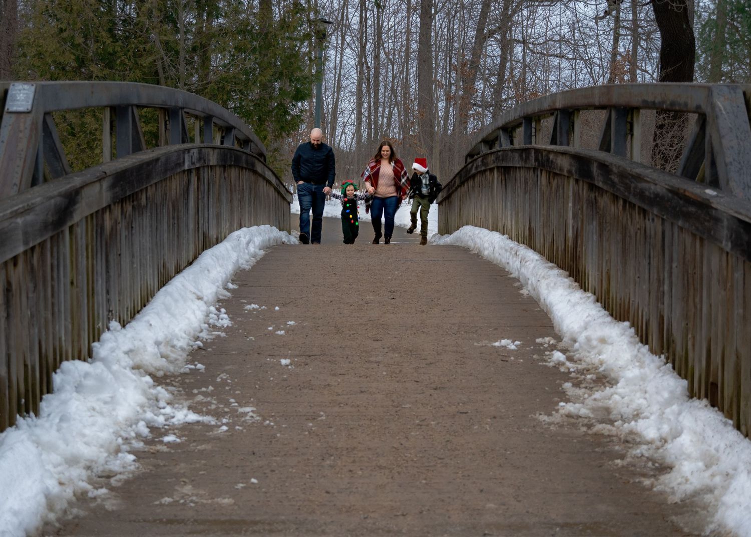 Snow-covered wooden walkway through winter forest with people visible in the distance.