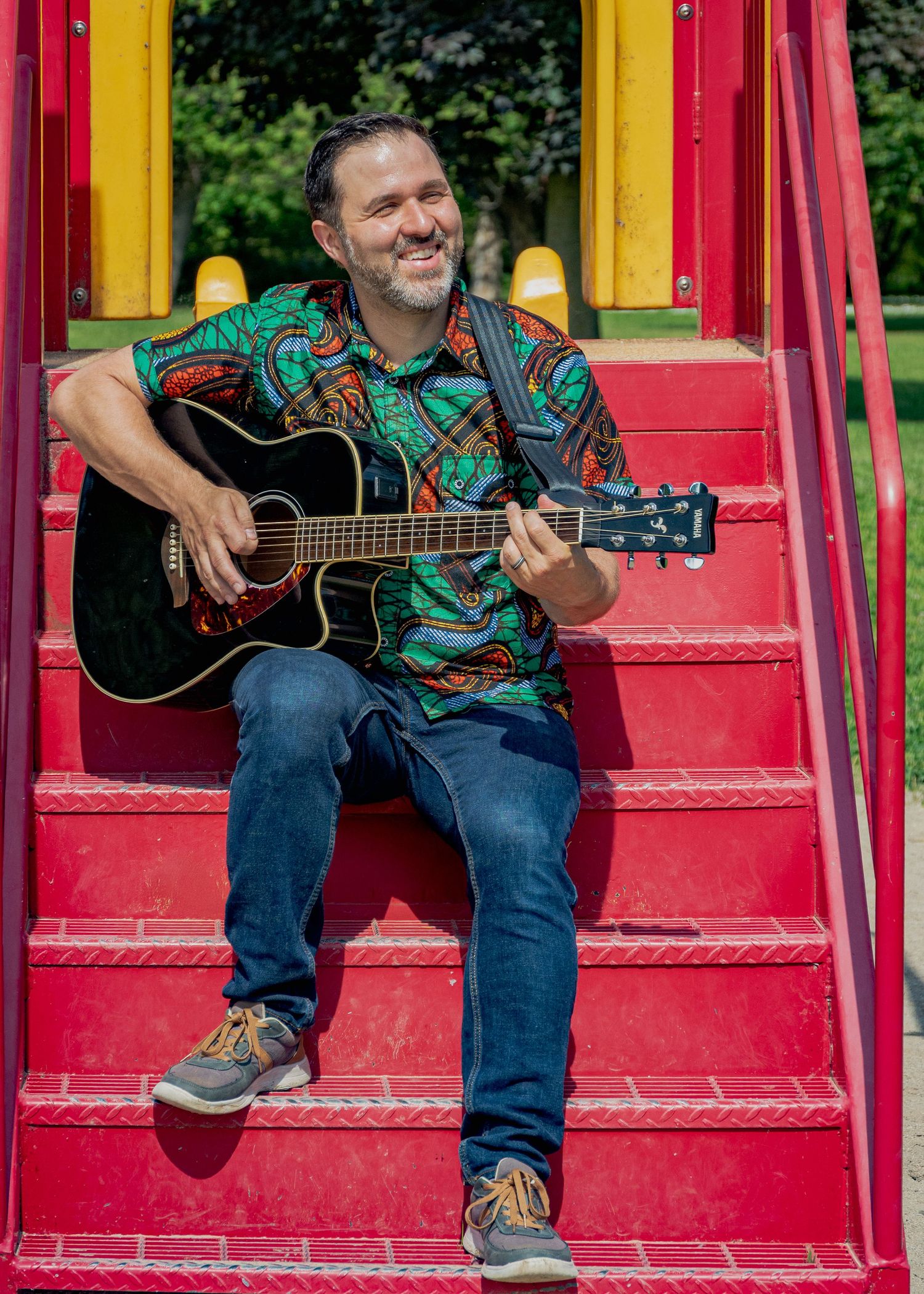 Musician playing guitar while sitting on red and yellow playground steps.