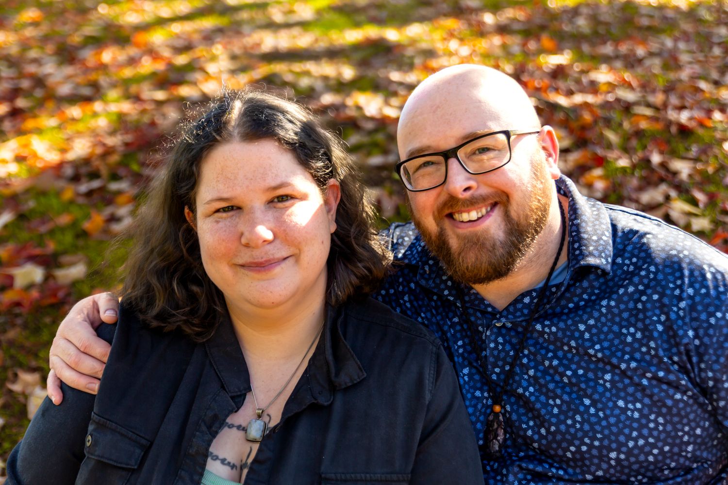 Candid outdoor photoshoot of a couple laughing together in fall foliage.