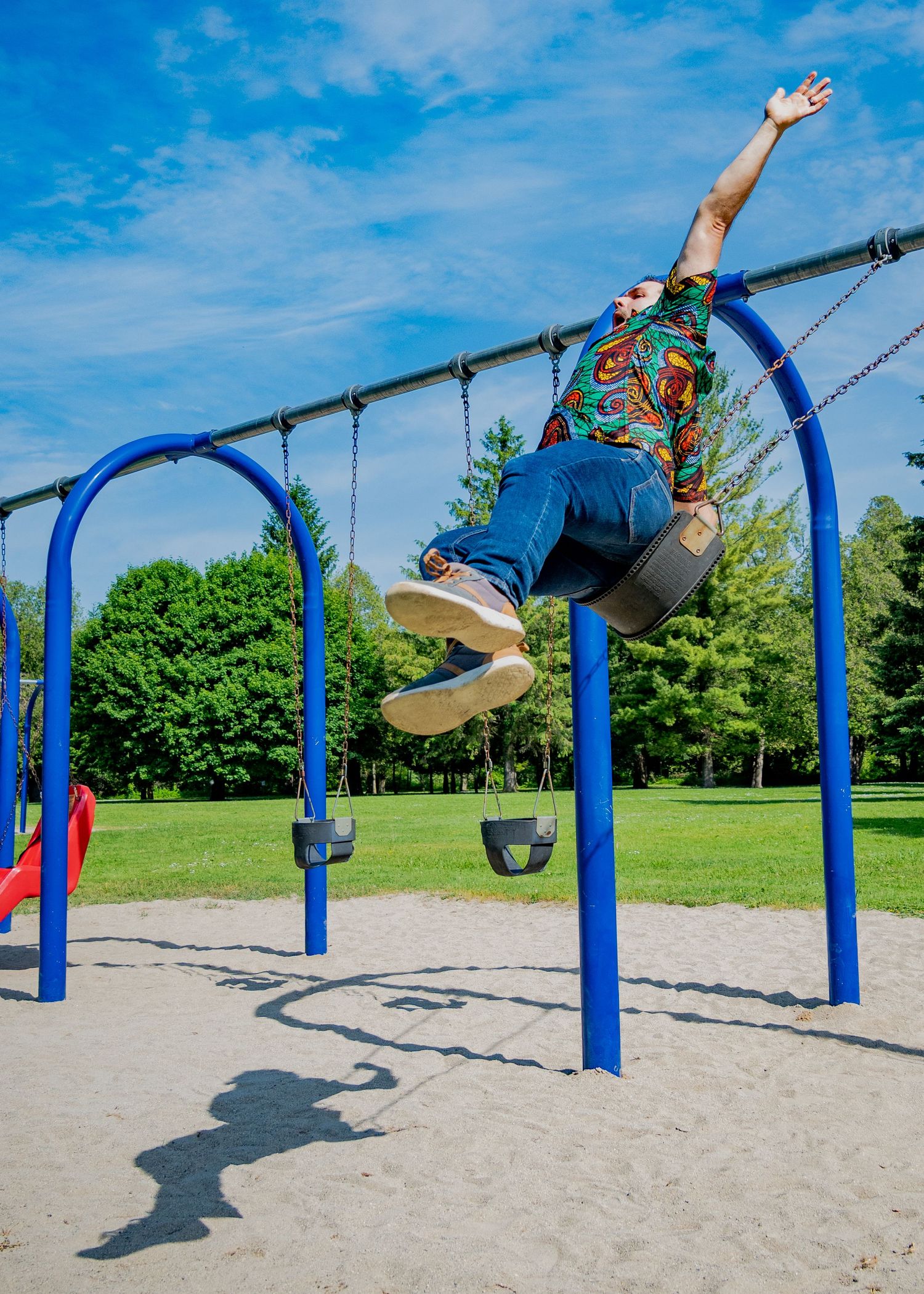 Action sequence of someone swinging high on blue playground swings against a bright summer sky.