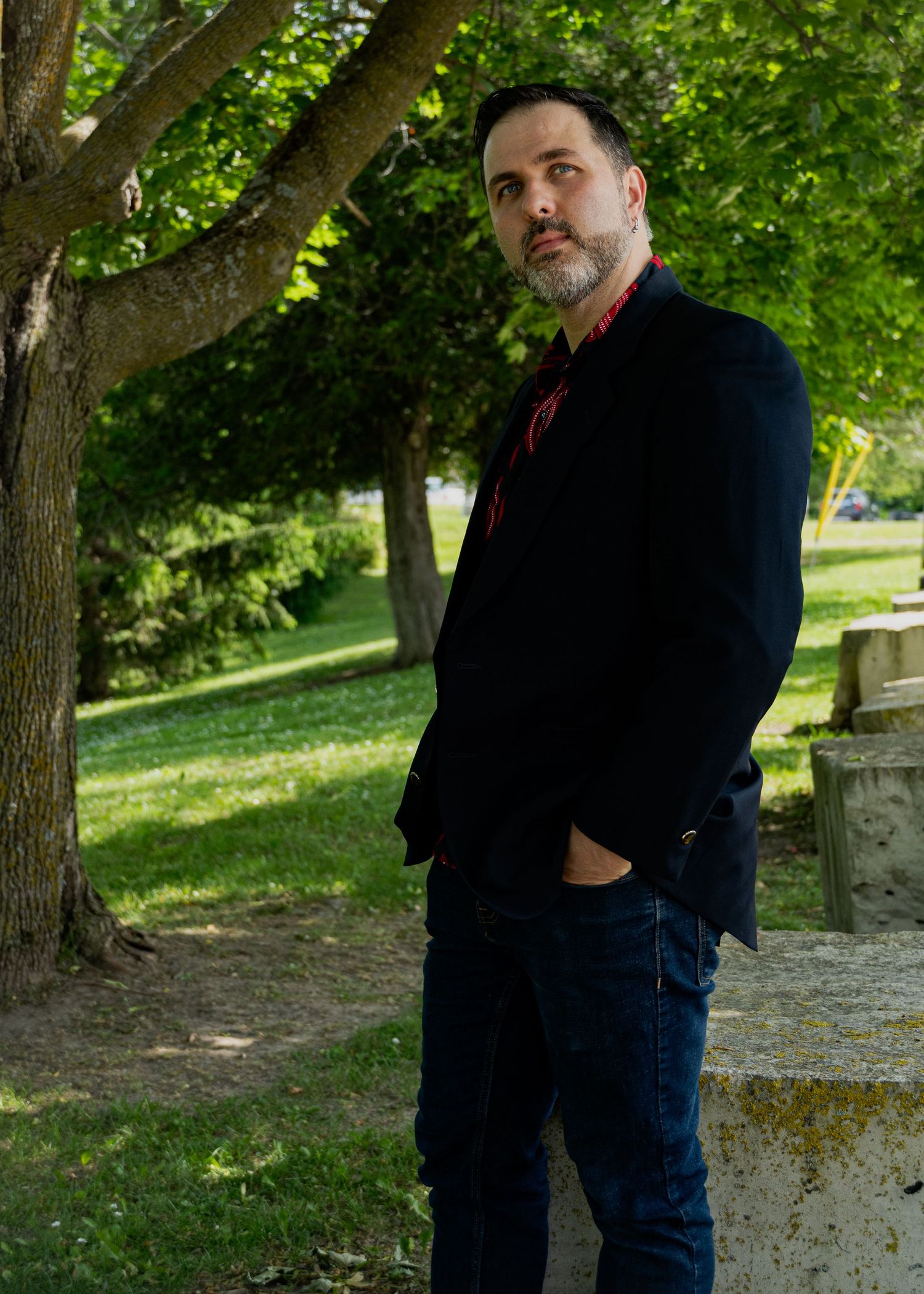 Person in dark clothing poses against lush green park backdrop with trees.