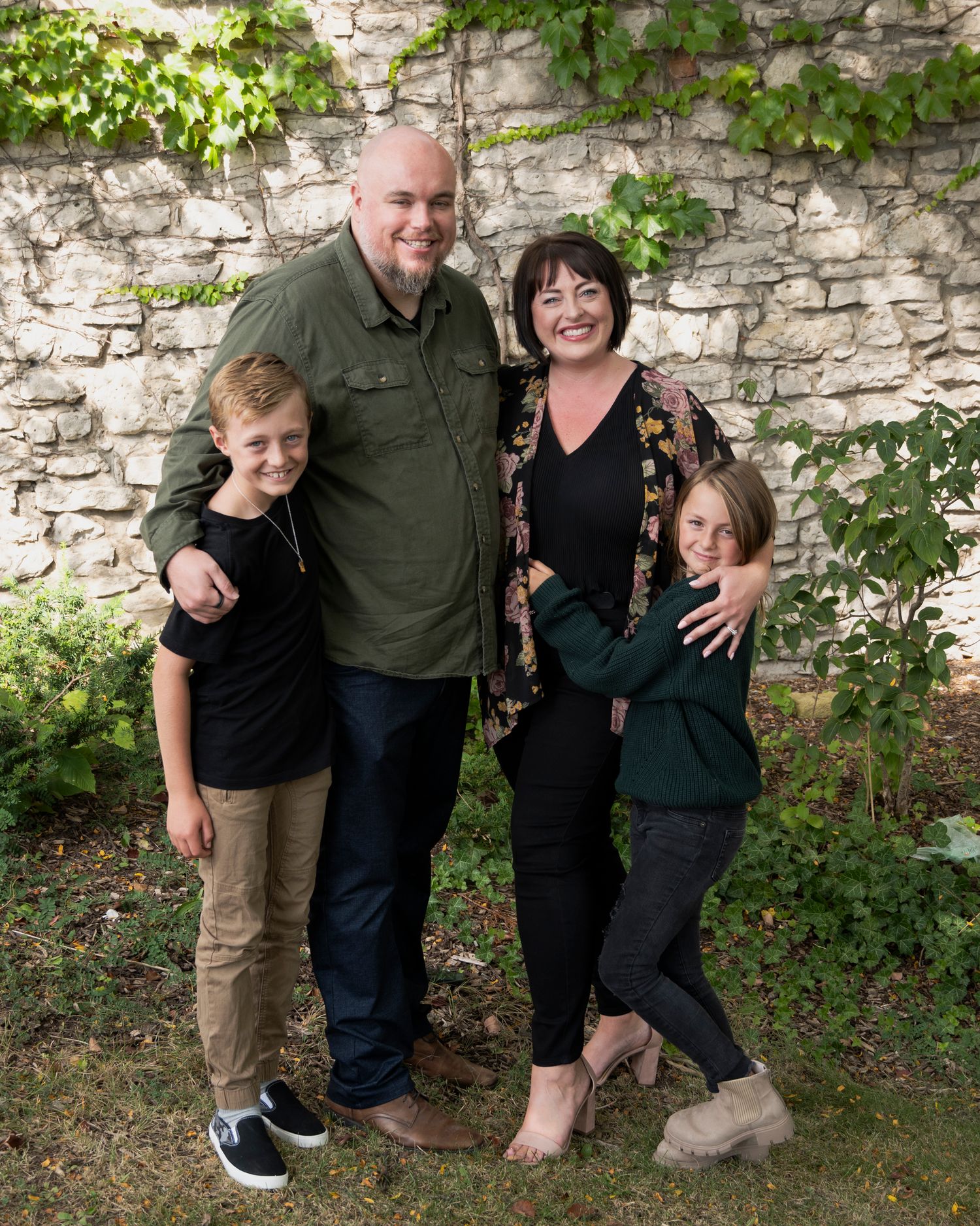 A family group poses casually together against a stone wall with ivy.
