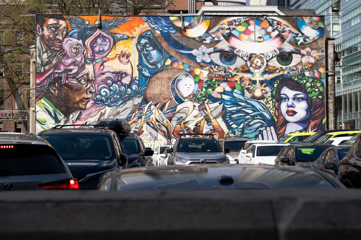 Street photography of a mural with the tops of cars in the foreground.
