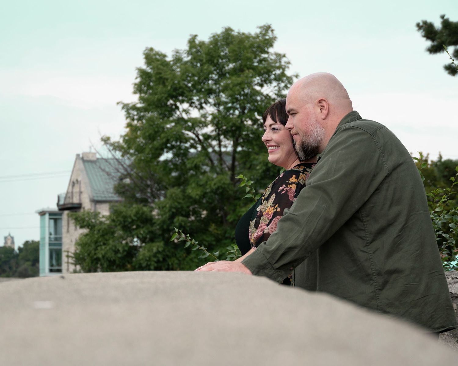 A couple sharing an intimate moment outdoors with trees and buildings in the background.