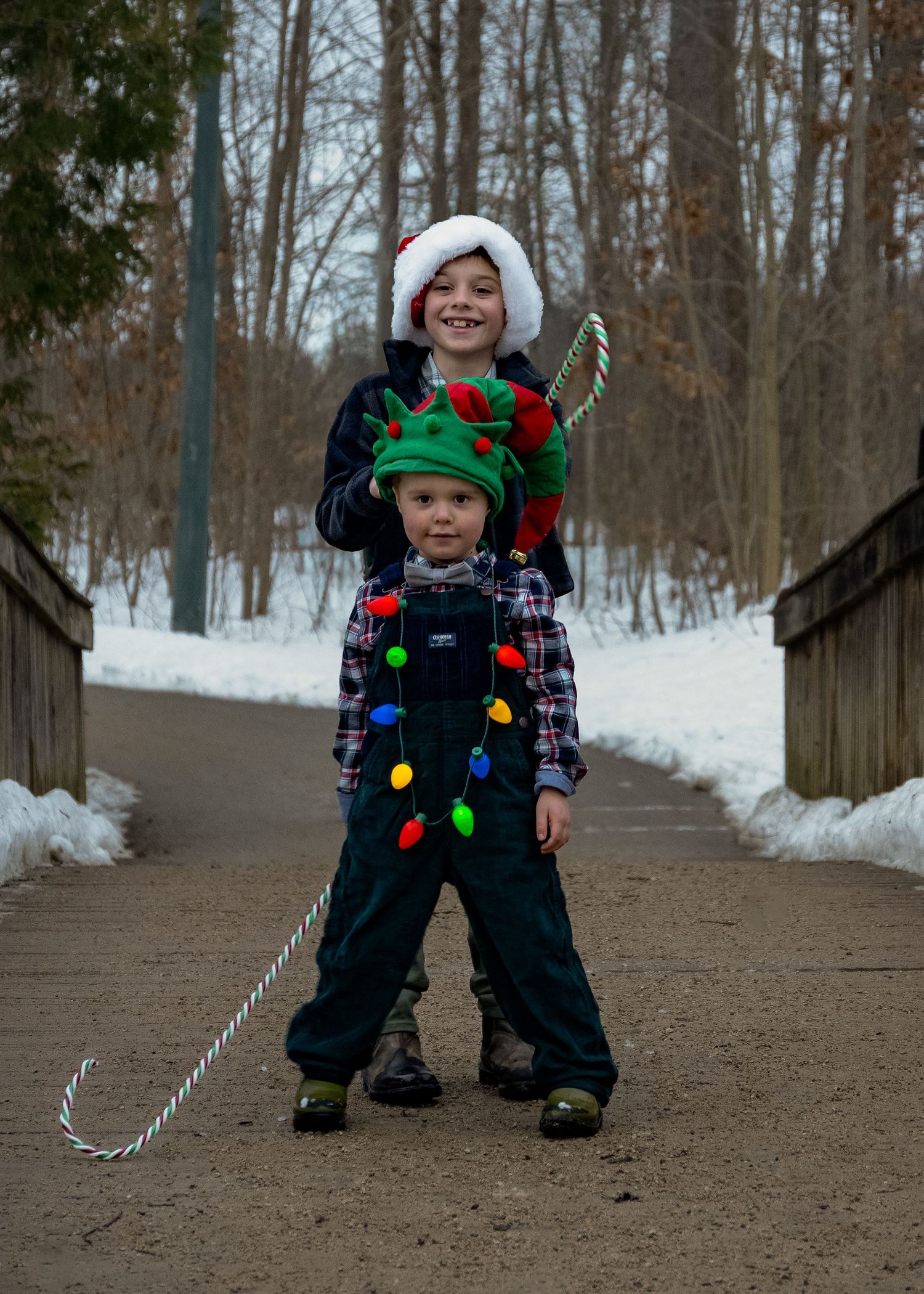 Children in winter clothes playing with holiday decorations on a wooden path.