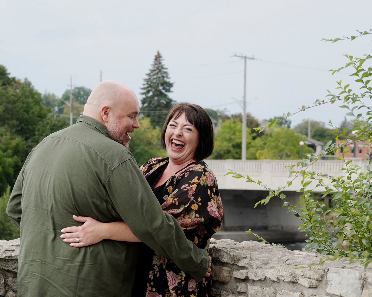 Couple embracing and laughing together by a stone wall outdoors.