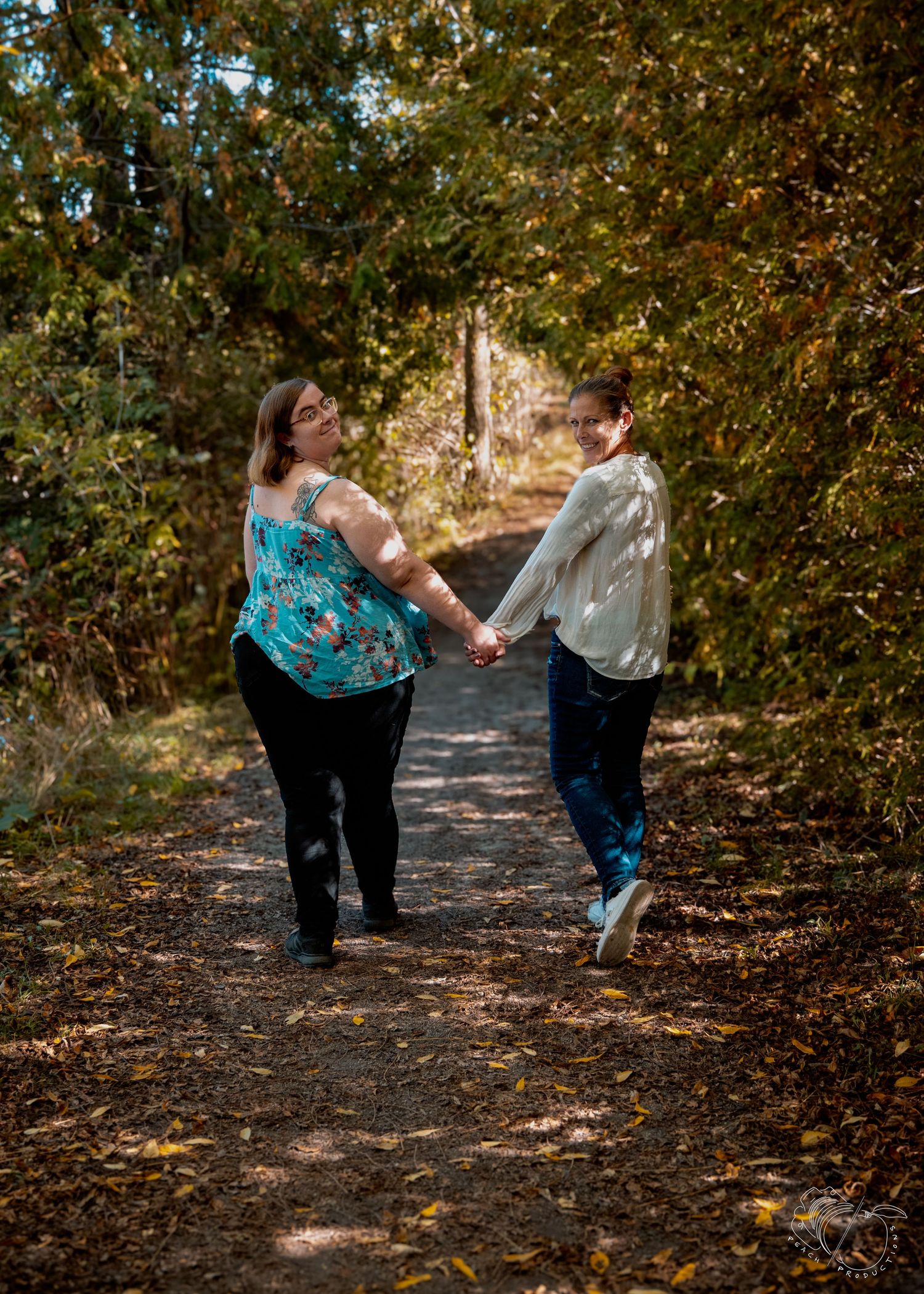 Two people walk and laugh together on a leaf-covered autumn path.