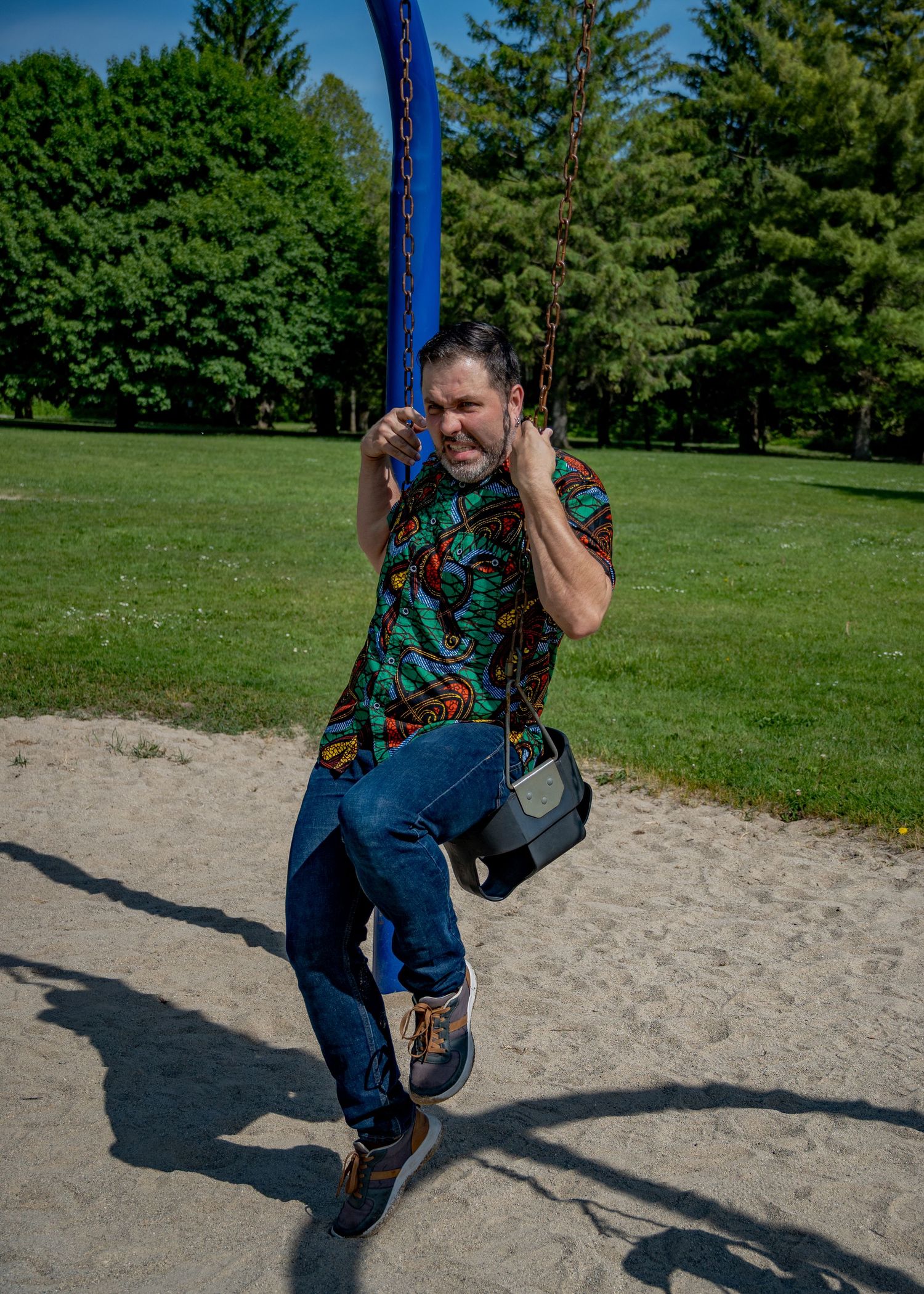 Person playing on playground swings in a park with green trees in the background.