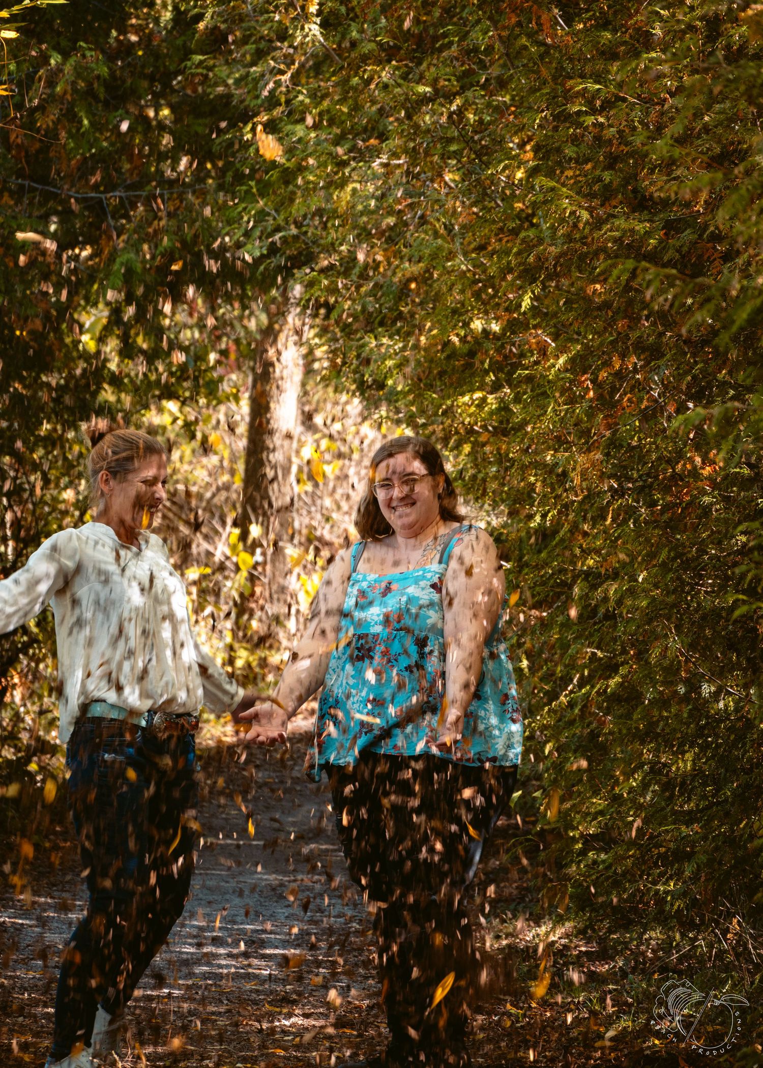 Autumn leaves fall around two people on stone steps surrounded by trees.