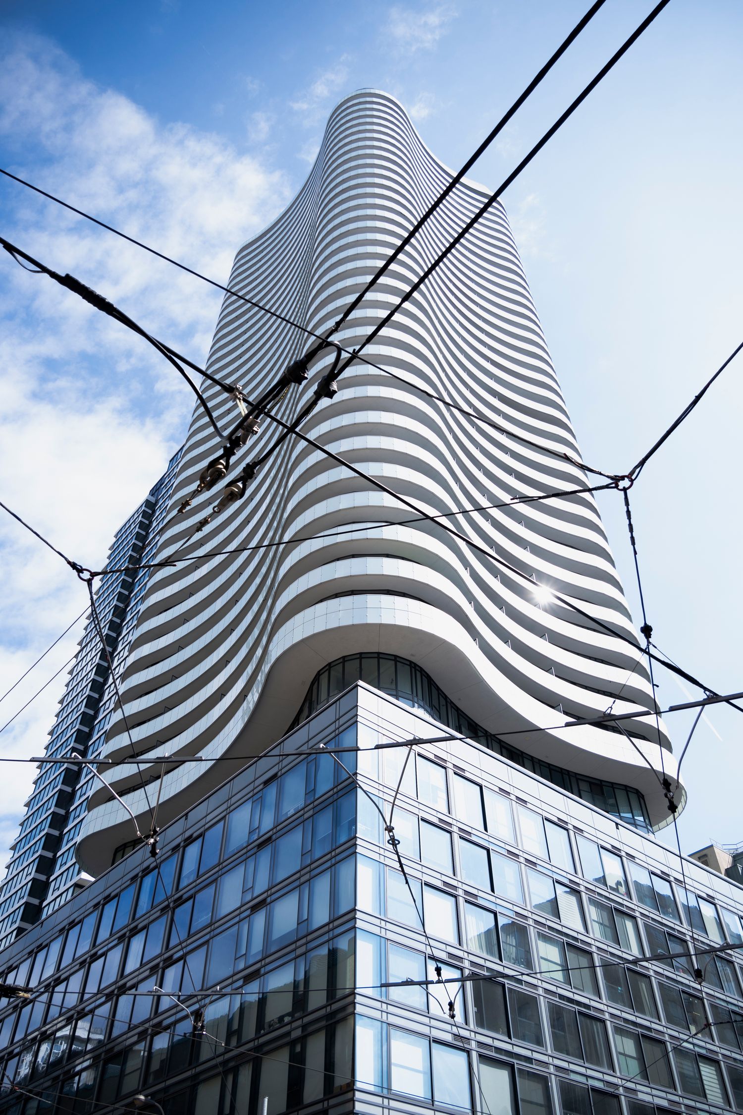 Street photography of a uniquely shaped building. Rail car lines and power lines criss cross in the foreground.