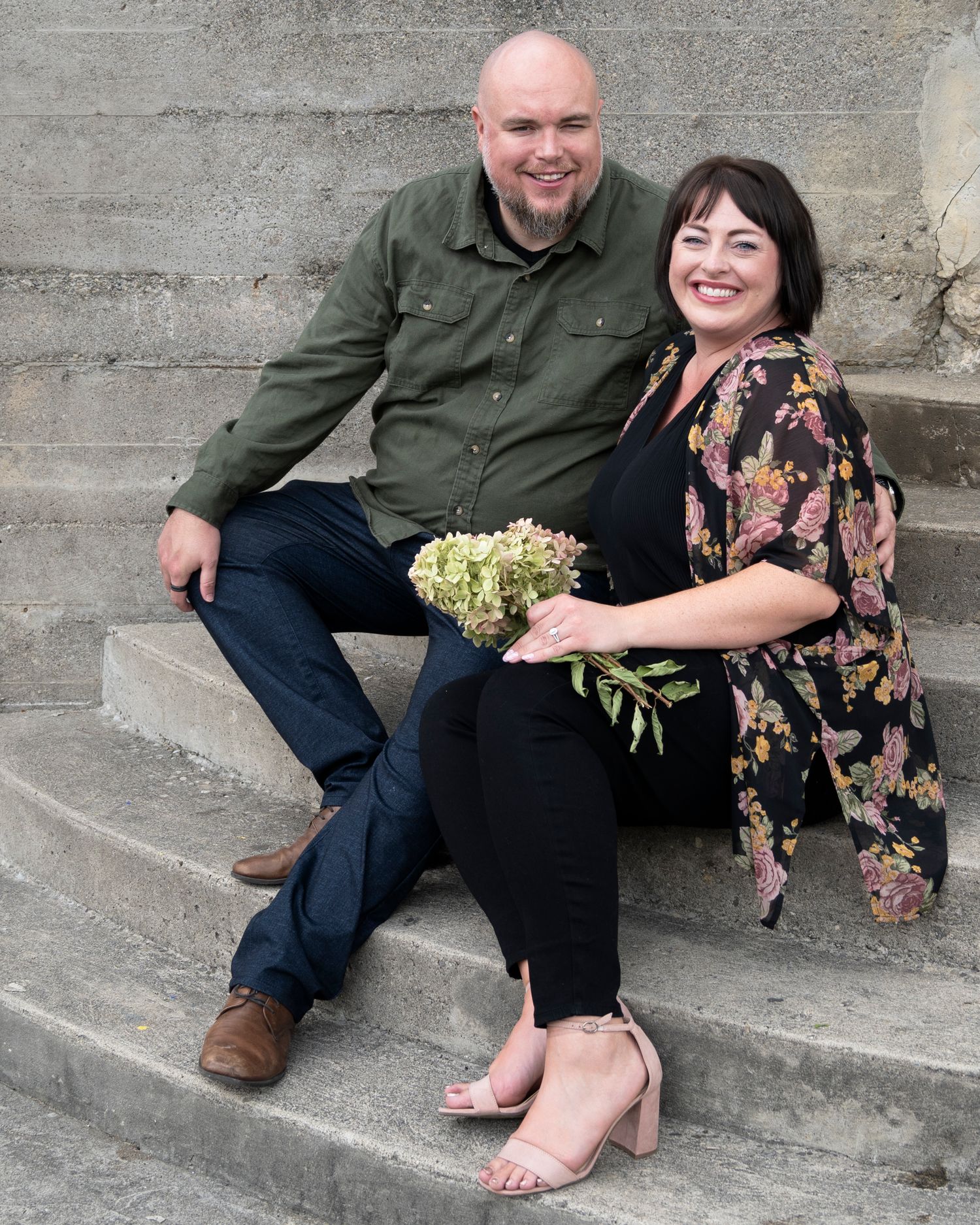 A couple sits casually on concrete steps sharing joyful moments together.