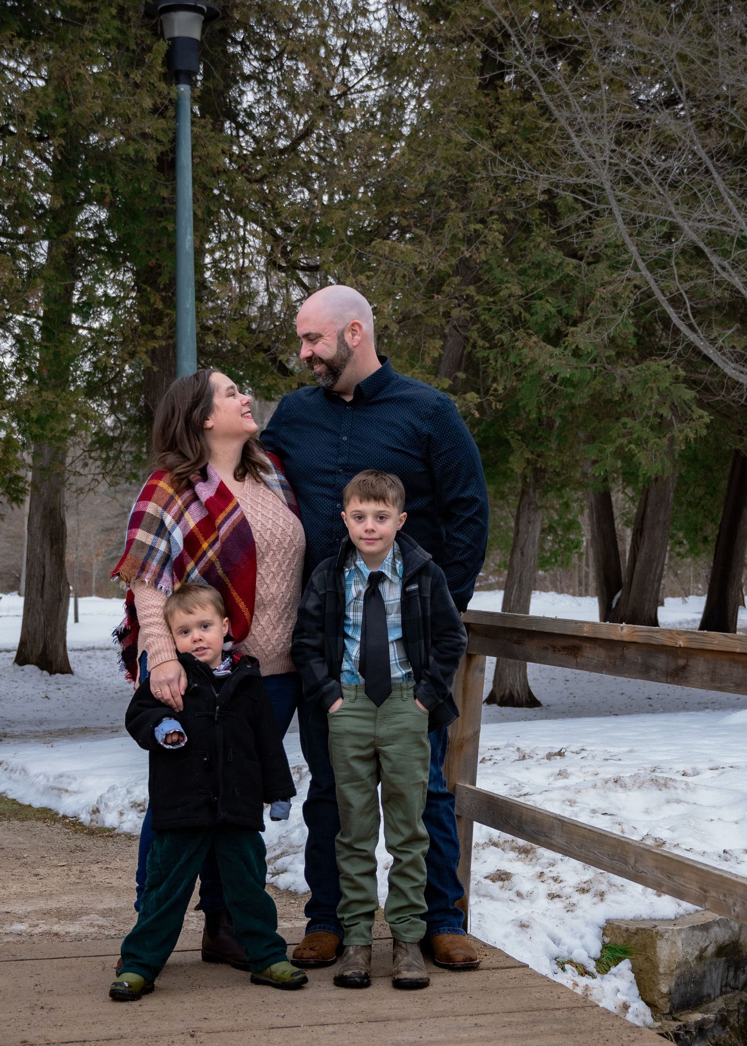 Family posing together on a wooden walkway during winter with snow covered ground in the background.