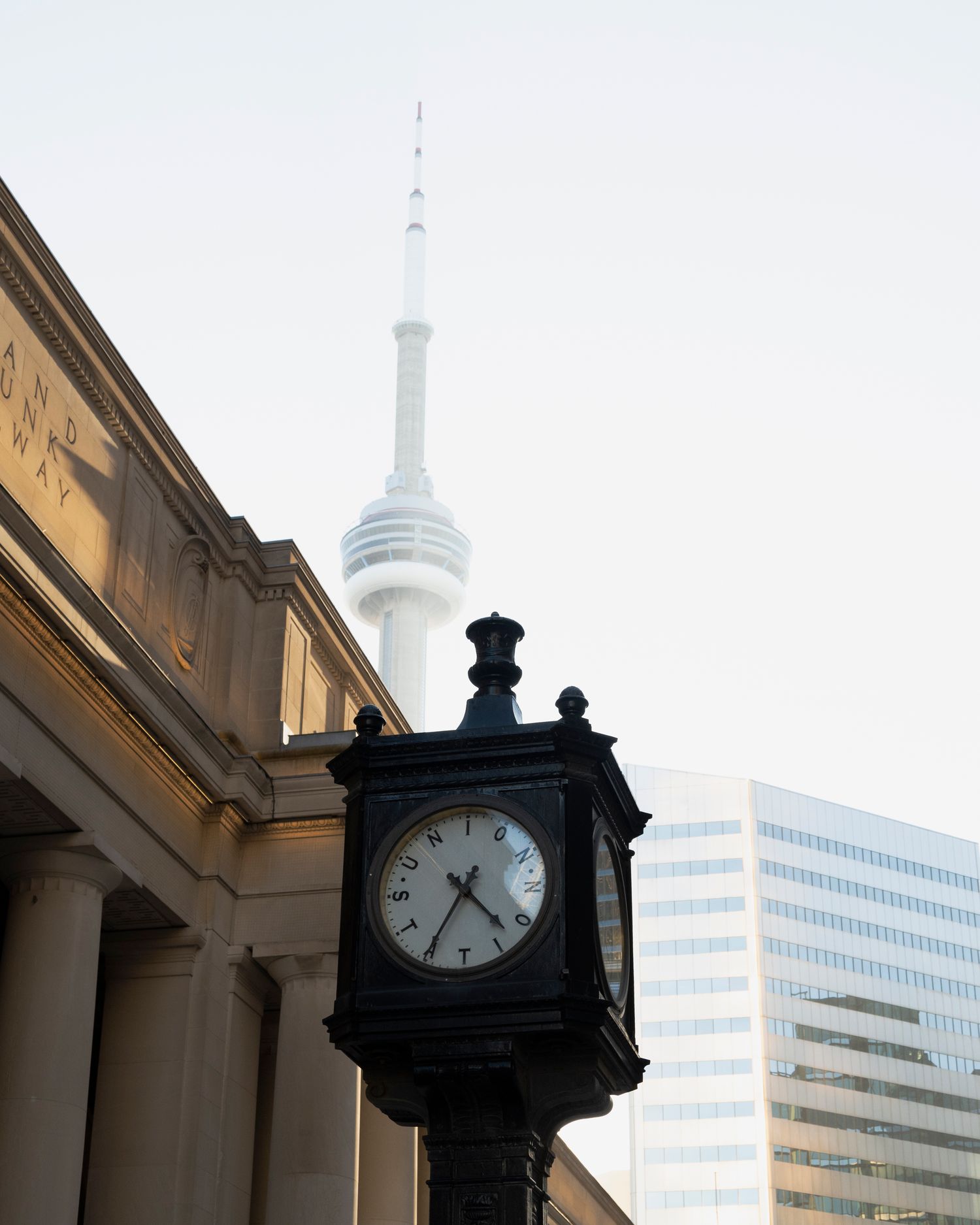 Street photography with a clock in the foreground and a misty CN Tower in the background.