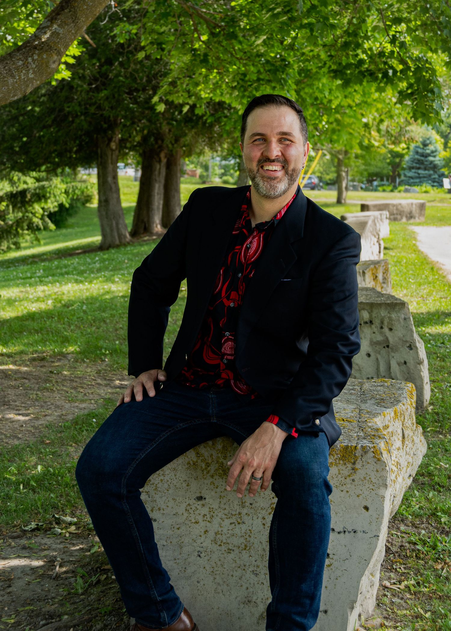 Person relaxing on stone bench surrounded by green trees in park setting.