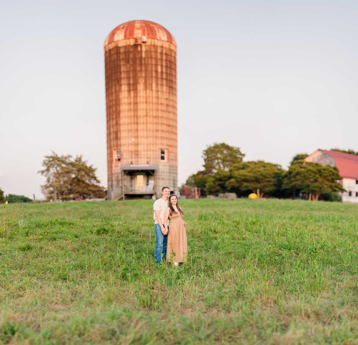Greensboro, NC Couples Photographer, Ryan Harden, Reidsville NC, loving couple holds each other in a lush green field at sunset at a silo.