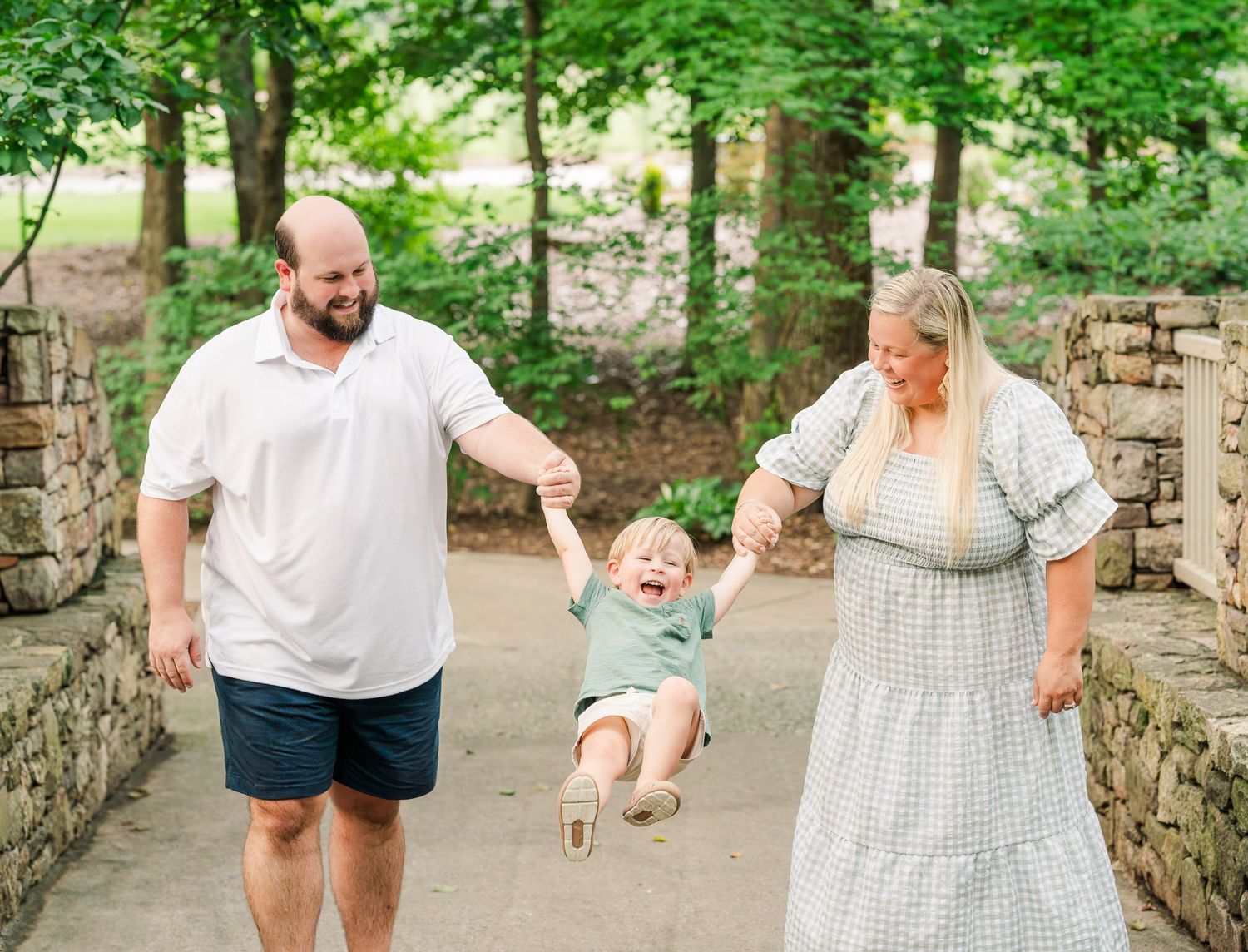 Greensboro, NC Family Photographer, Ryan Harden, Reidsville NC, happy family swings son on walking path Tanger Family Bicentennial Gardens