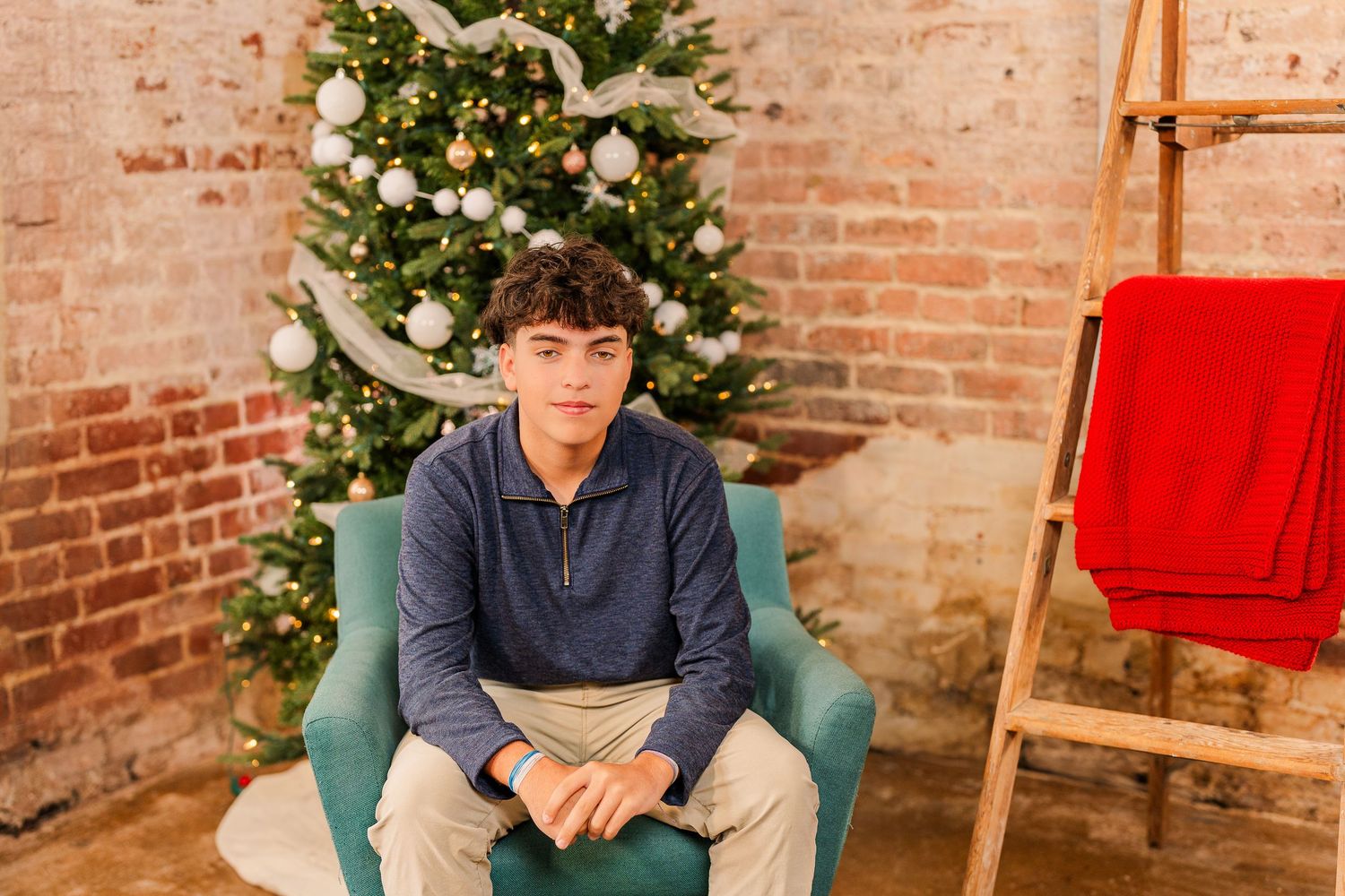 Greensboro, NC Family Photographer, Ryan Harden, Reidsville NC, son poses in front of Christmas tree for seasonal session in studio.