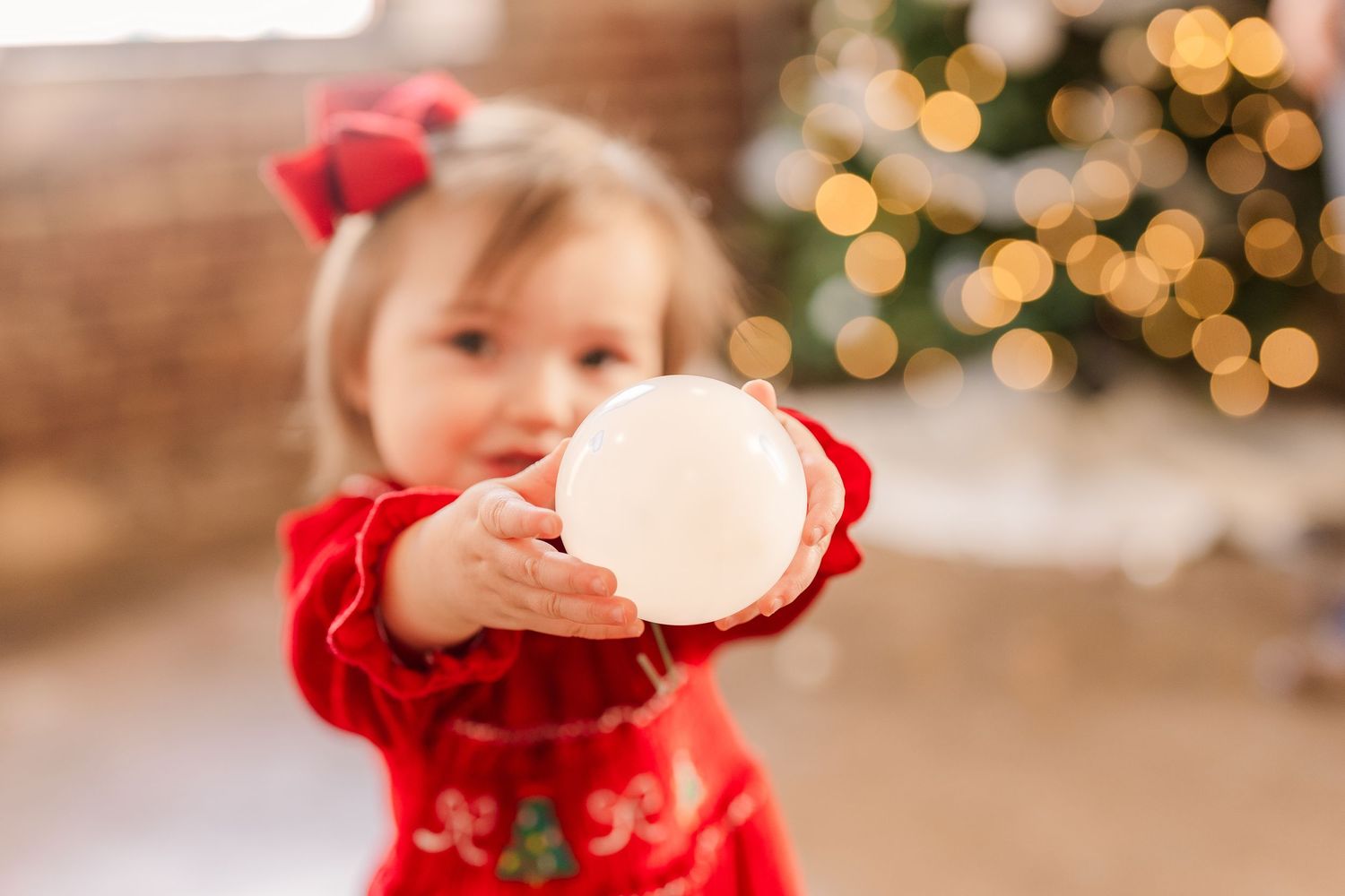 Greensboro, NC Family Photographer, Ryan Harden, Reidsville NC, child holds ornament in front of Christmas tree for seasonal session.