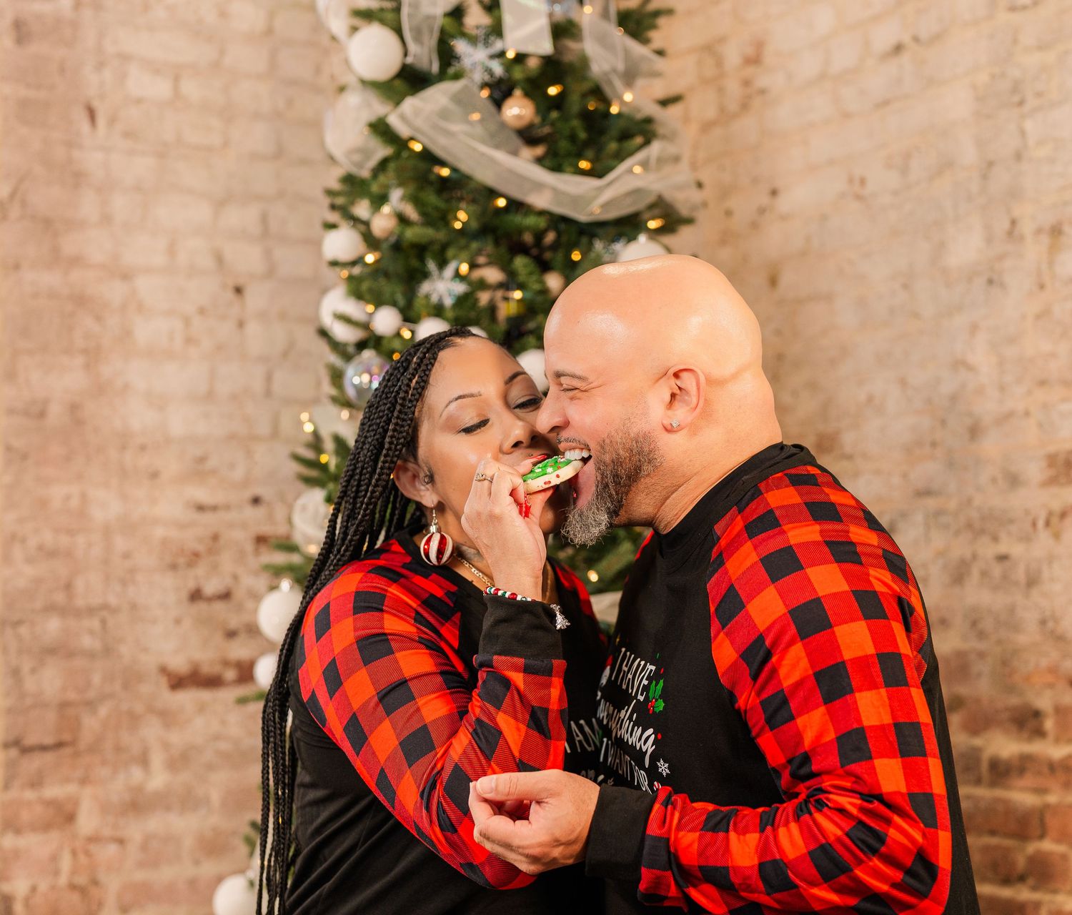 Greensboro, NC Couples Photographer, Ryan Harden, Reidsville NC, Happy couple poses in front of Christmas tree eating a cookie.