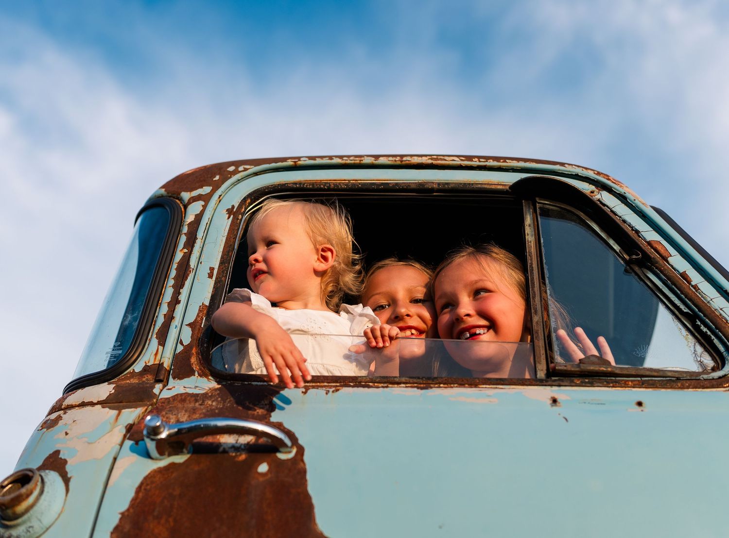 Greensboro, NC Family Photographer, Ryan Harden, Reidsville NC.  Three children playing in old light blue truck with bright blue sky.