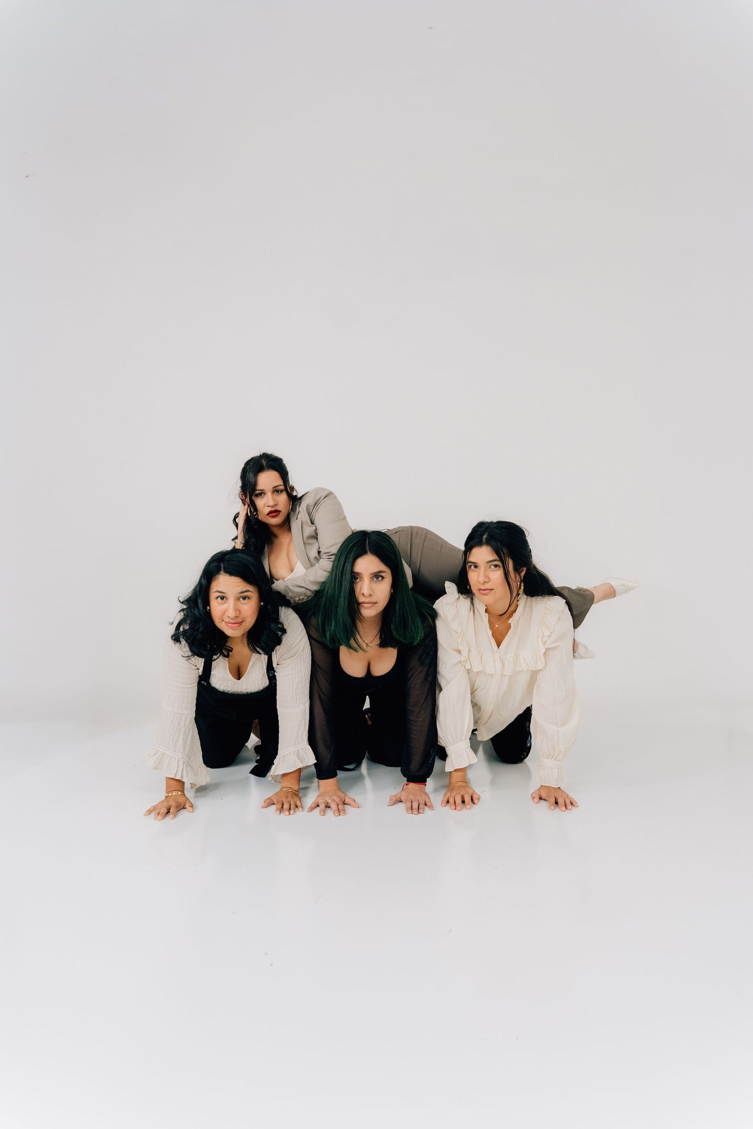 Four women pose playfully on the floor in a minimalist white studio setting wearing casual black and white outfits.