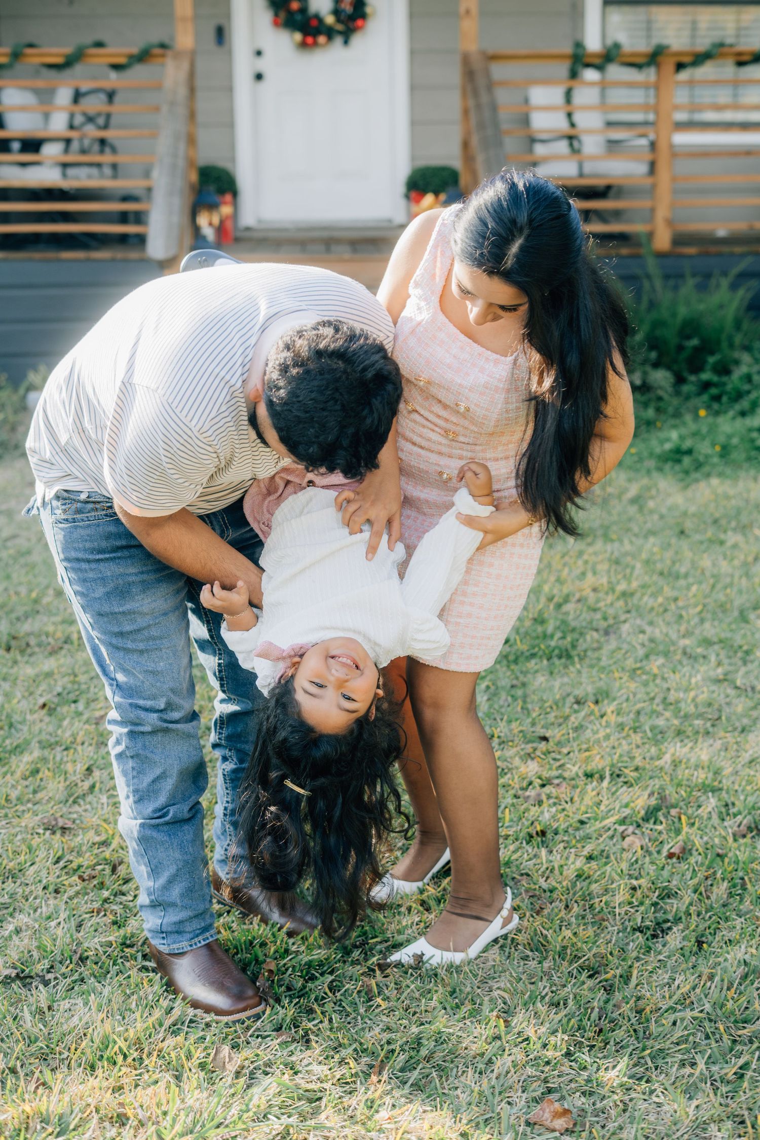 Family playing and laughing together on grass outside their home.