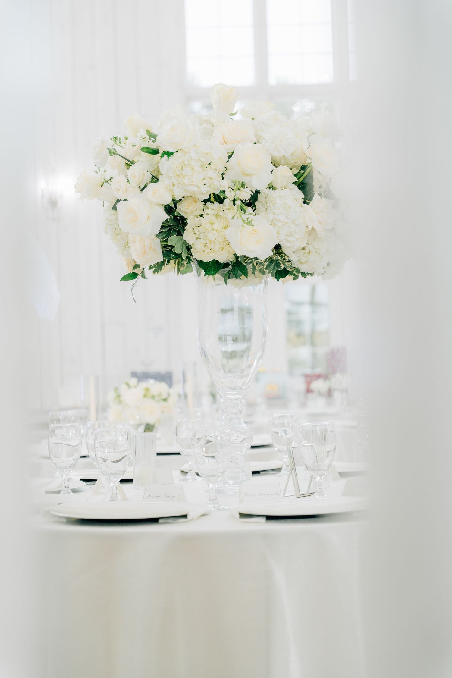 Elegant white floral centerpieces and glassware on wedding reception tables.