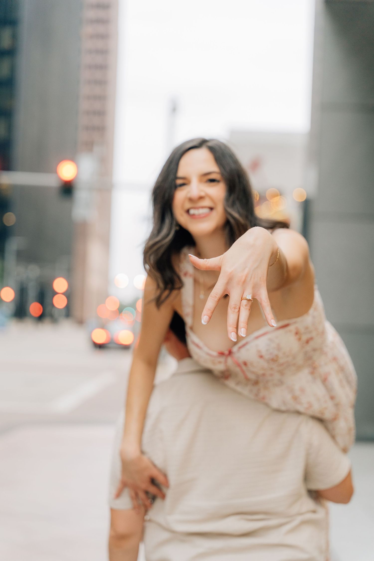A woman in a flowy beige dress twirls and dances gracefully on a city street at dusk.