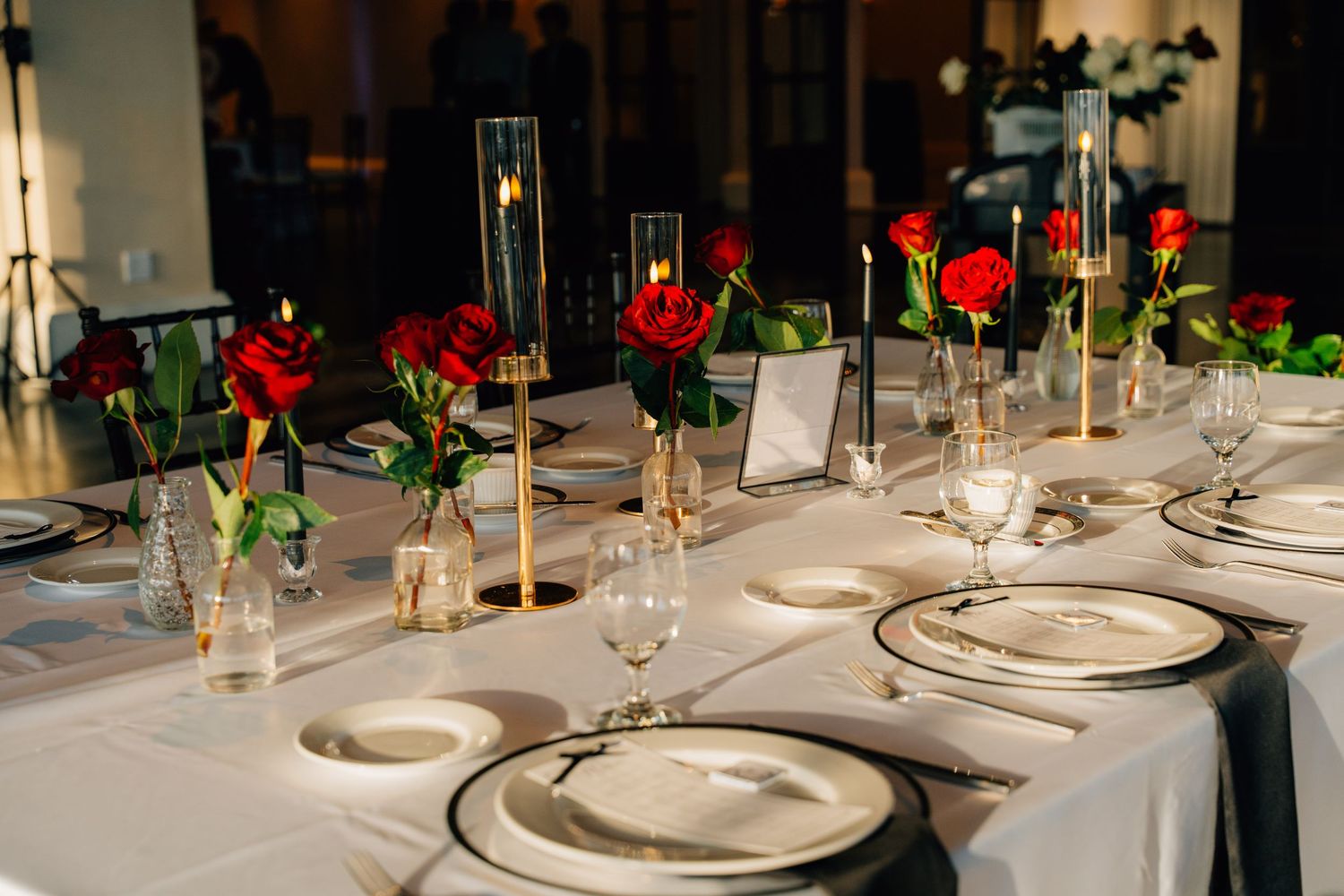 Elegant wedding reception table settings with red roses and candles create a romantic atmosphere.