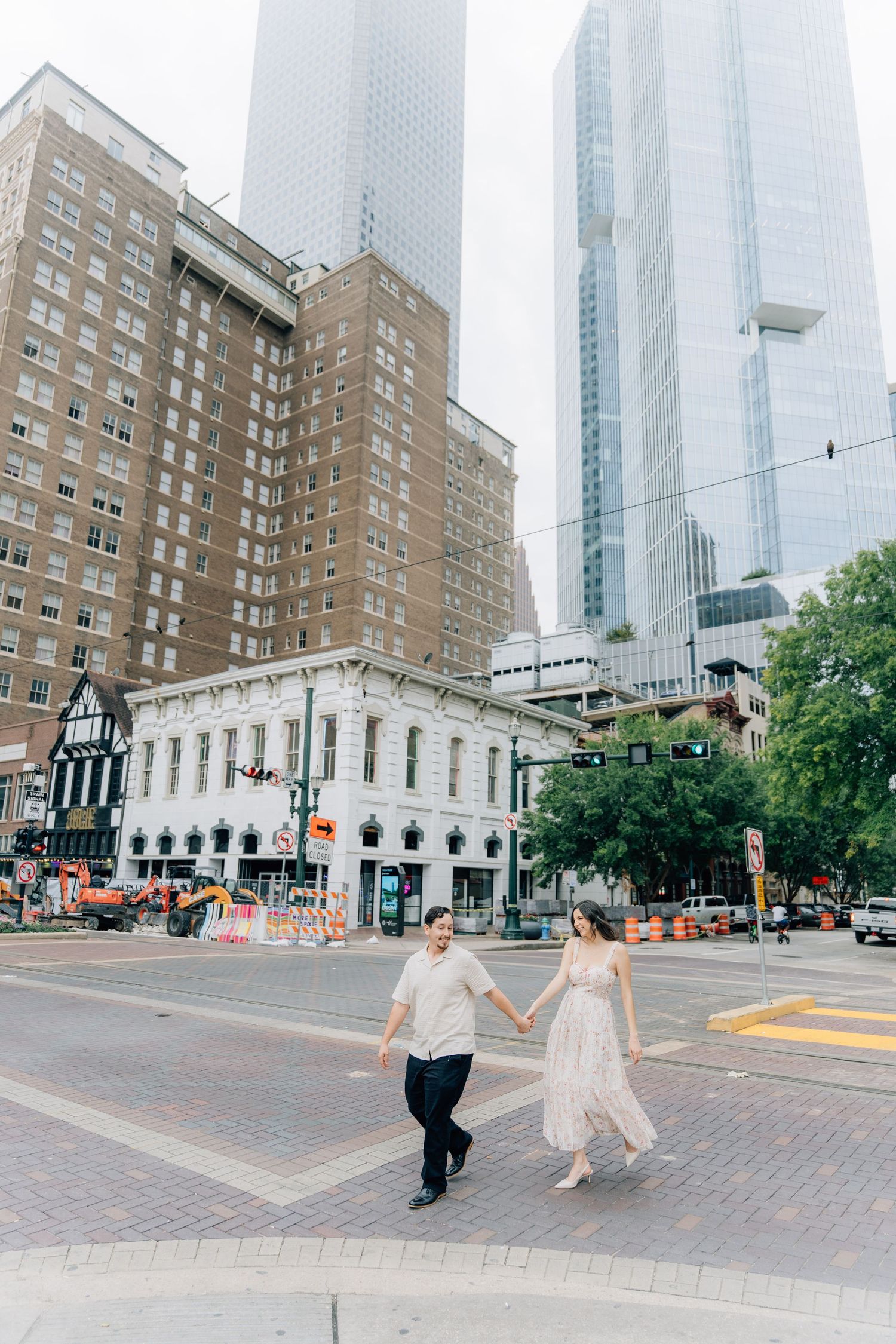 A couple holding hands while walking through downtown streets with skyscrapers towering above.