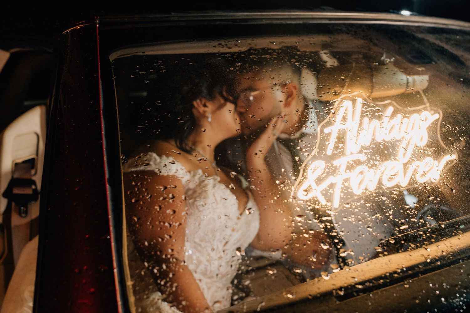 Romantic car moment with neon 'Just Married' sign visible through rain-spotted window.