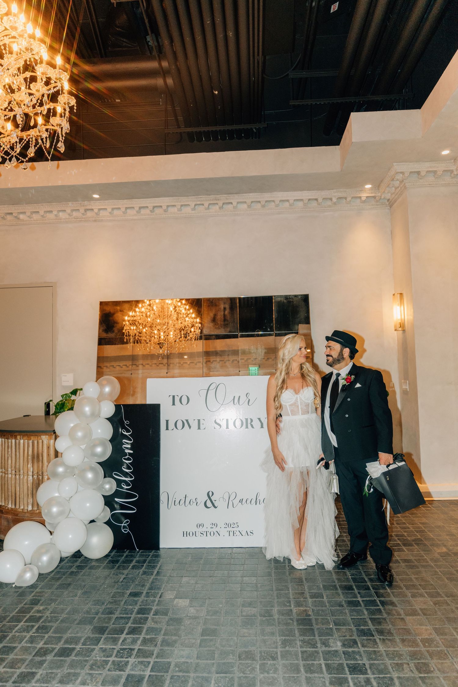 Wedding reception space decorated with white balloons, chandeliers, and custom signage.