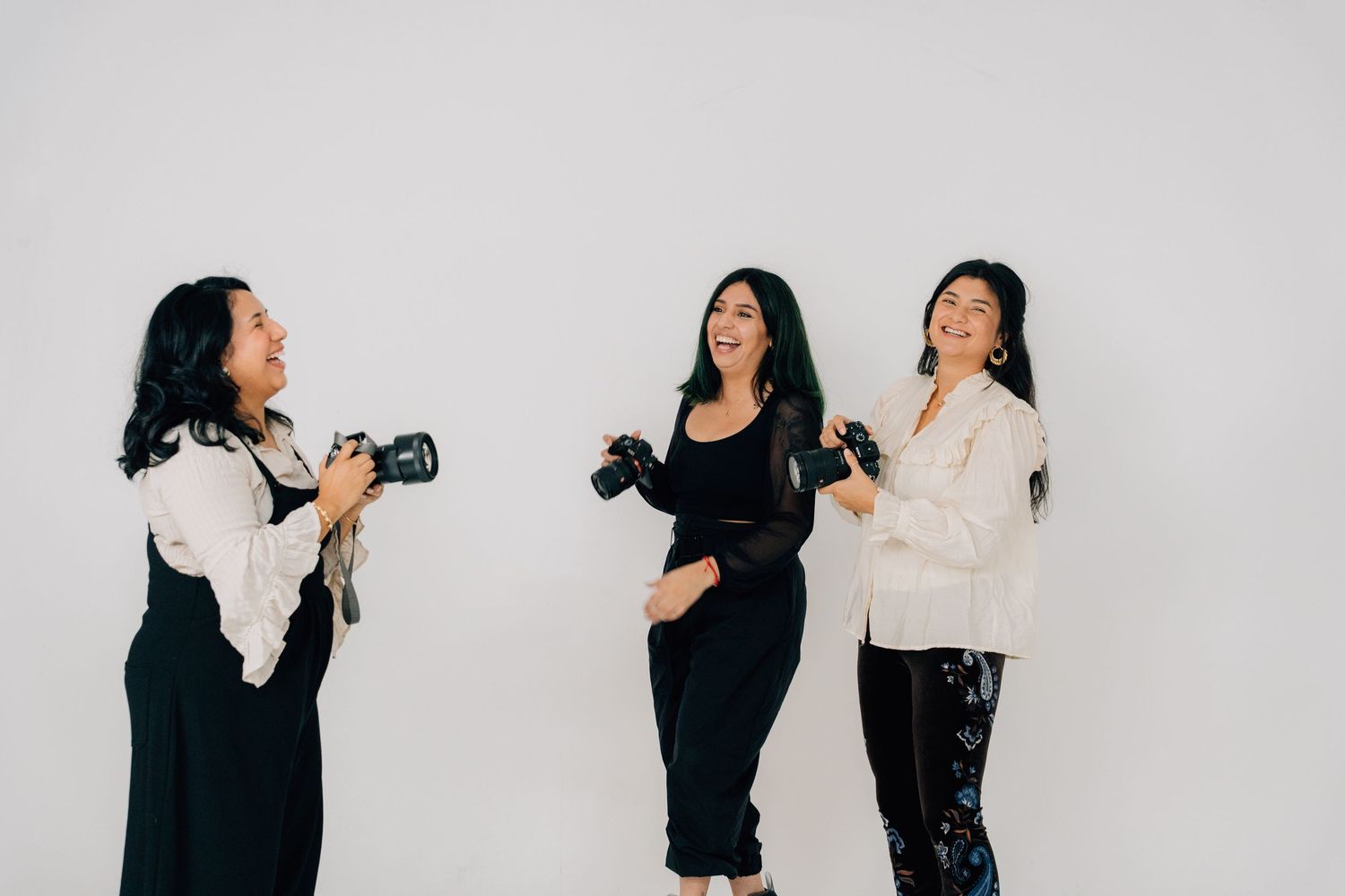 Three photographers interact and take photos of each other against a white backdrop.