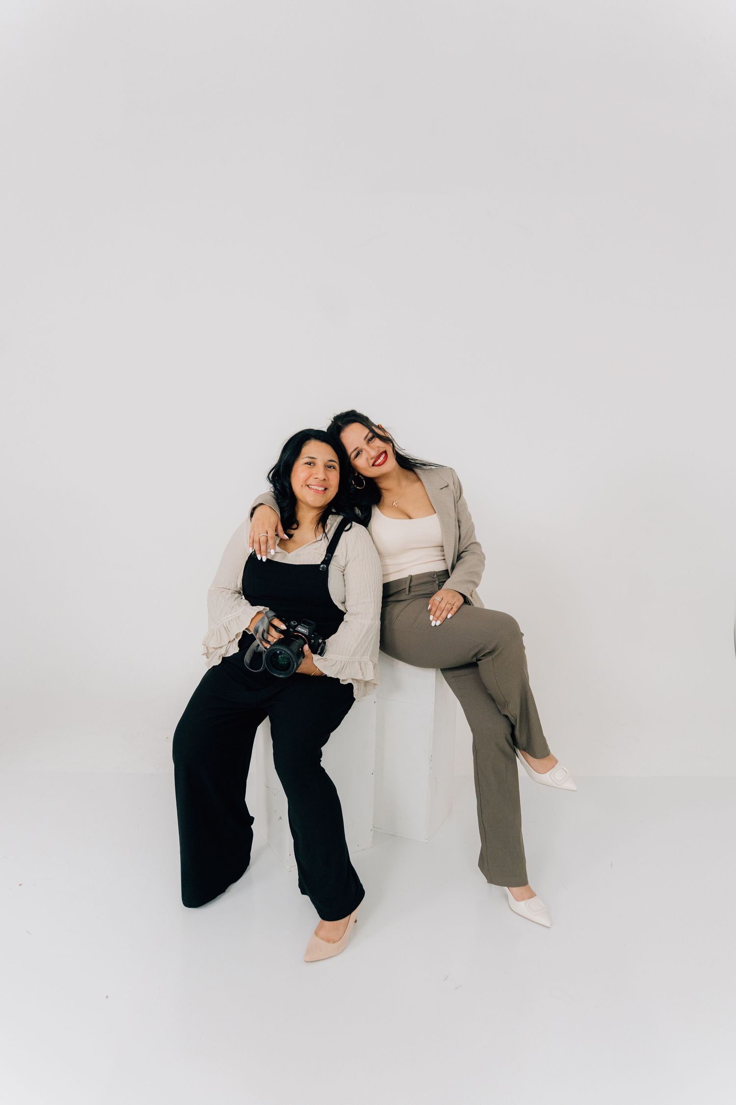 Two people in contrasting outfits pose playfully together on a white studio floor.