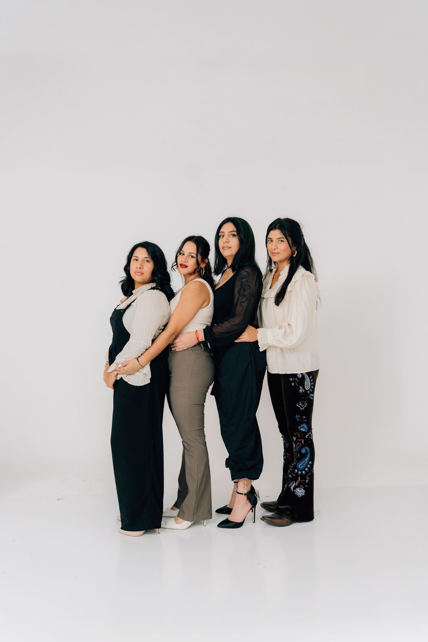 Four women stand in line wearing coordinated neutral-toned outfits against white background.